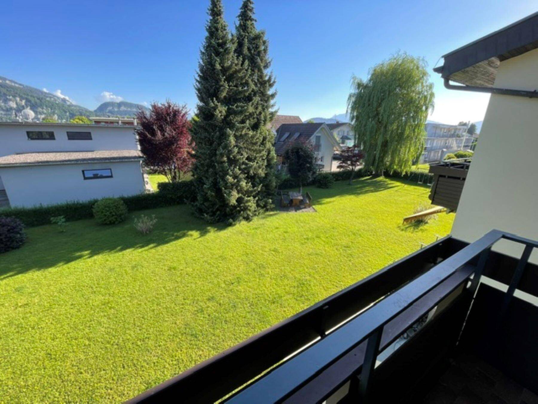 Panoramablick vom Balkon auf den gepflegten Rasen, Bäume und die Bergkulisse.