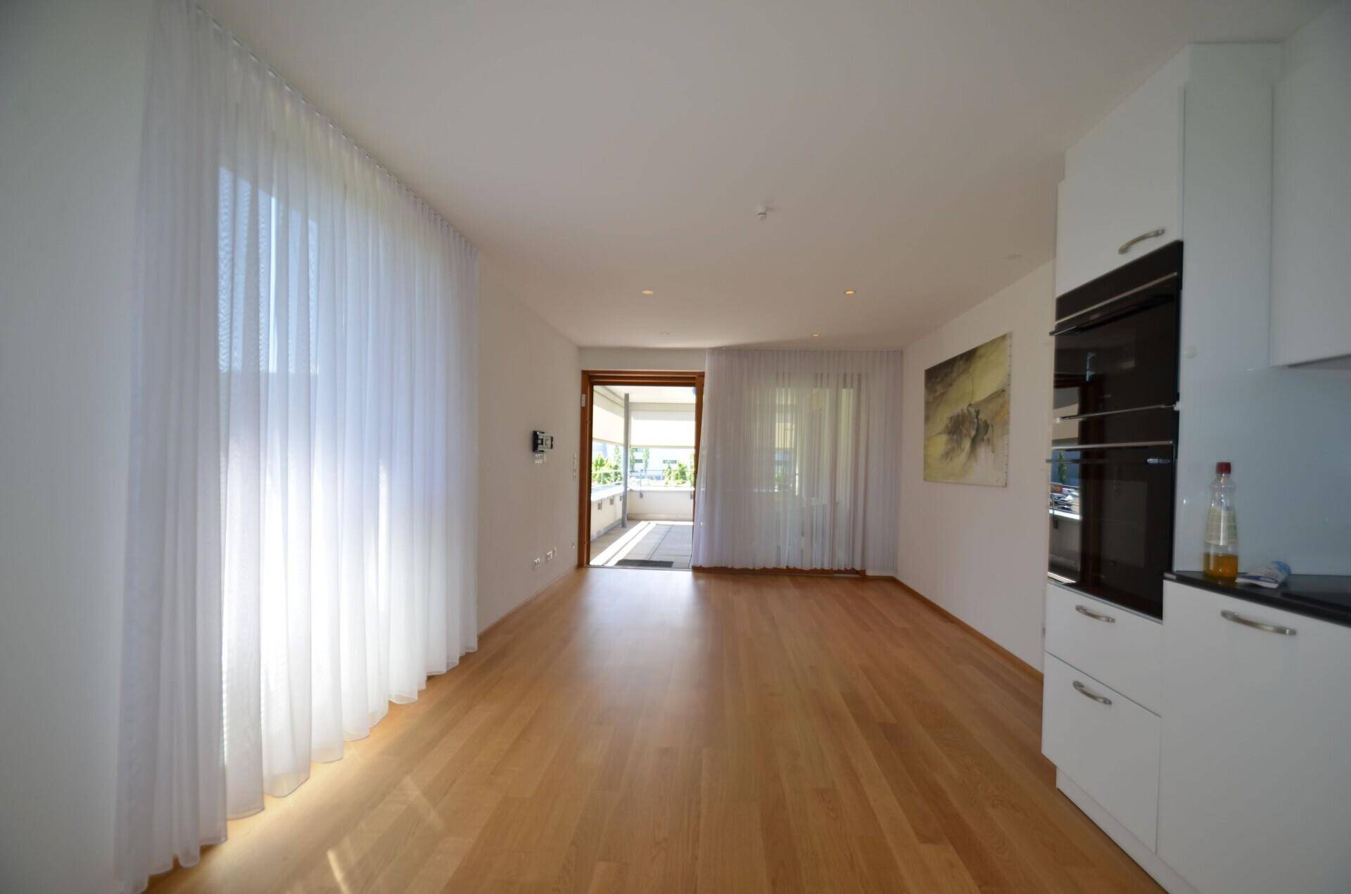 Lichtdurchfluteter Wohnbereich mit Holzboden, offener Küche und direktem Zugang zum Balkon.