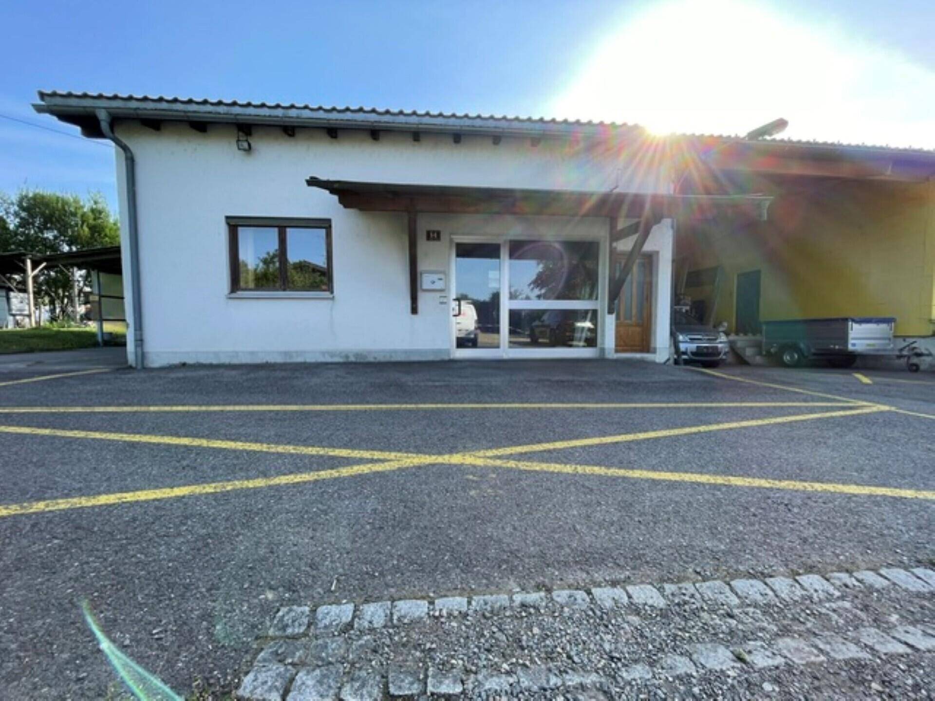 Außenansicht eines weißen Gebäudes mit großem Parkplatz und gelben Markierungen unter strahlendem Sonnenschein.