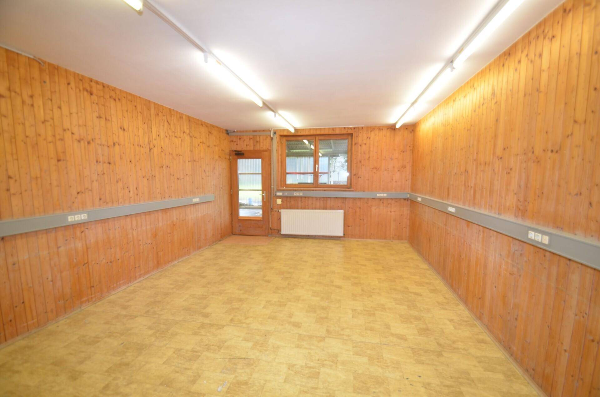 Heller Raum mit Holzvertäfelung, Linoleumboden und einer Tür, die ins Freie führt, sowie einem Fenster.