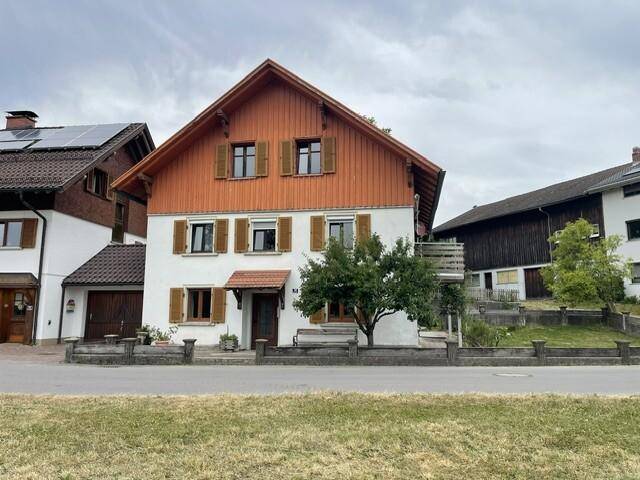 Traditionelles Haus mit weißer Fassade, Holzverkleidung und braunen Fensterläden unter bewölktem Himmel.