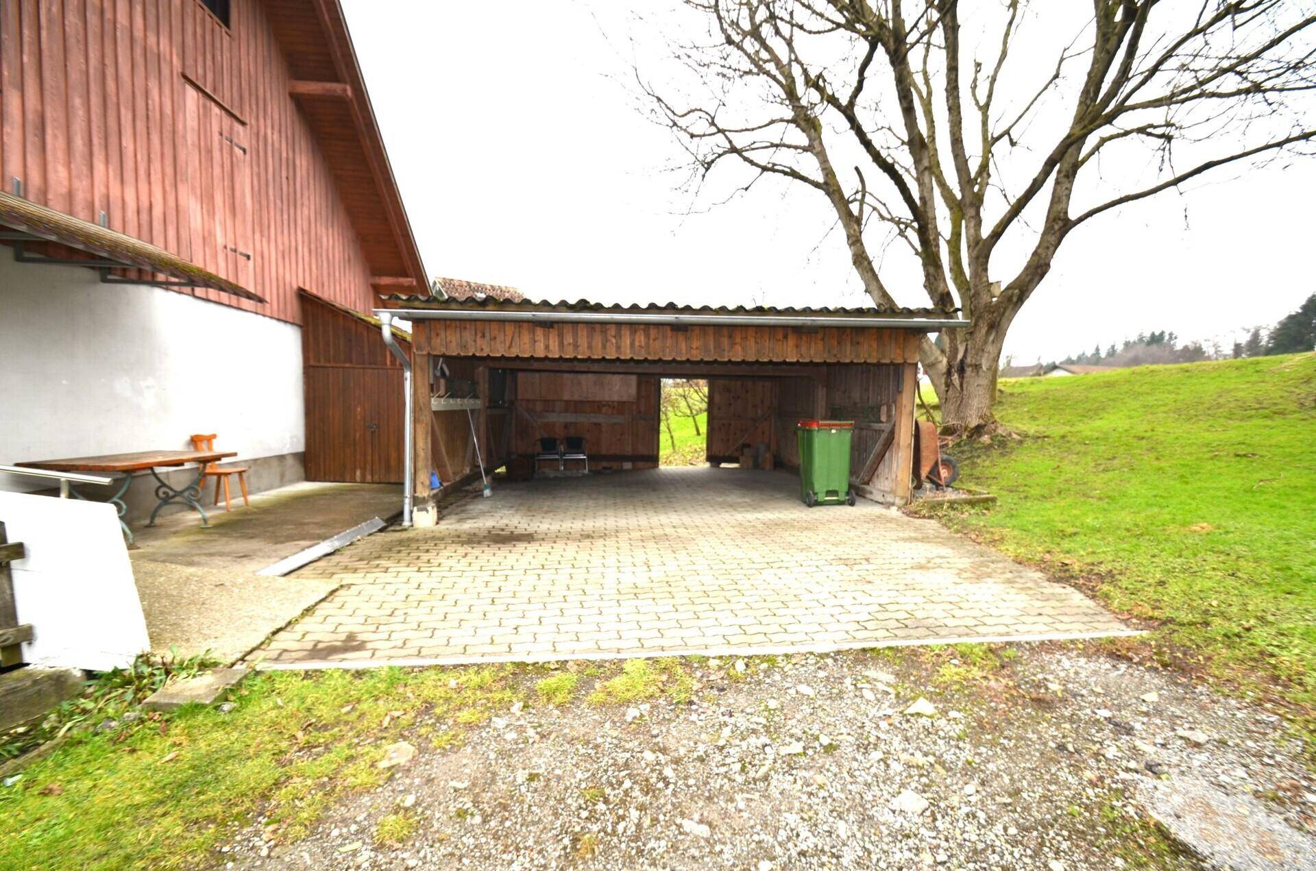 Geräumiger Carport mit gepflasterter Fläche und angrenzendem Holzschuppen.