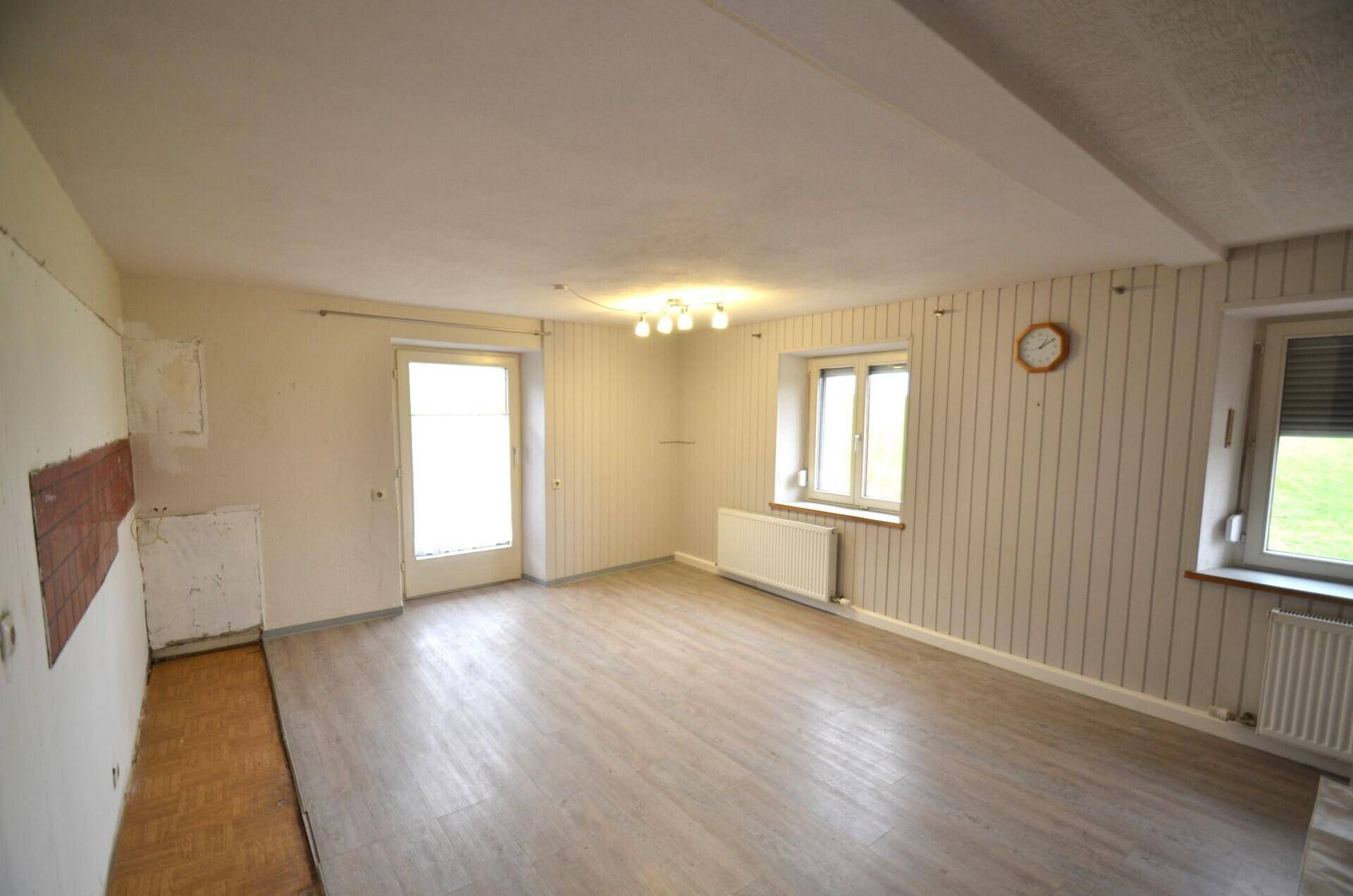 Geräumiges Zimmer mit Laminatboden, Tapeten und Zugang zu einem Außenbereich.