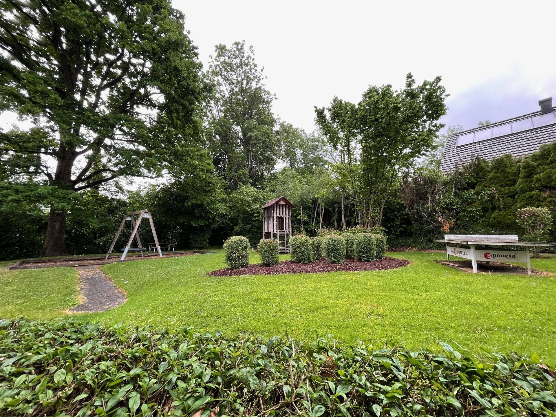 Großer Garten mit Spielplatz, Tischtennisplatte und altem Baumbestand, perfekt für Familien.