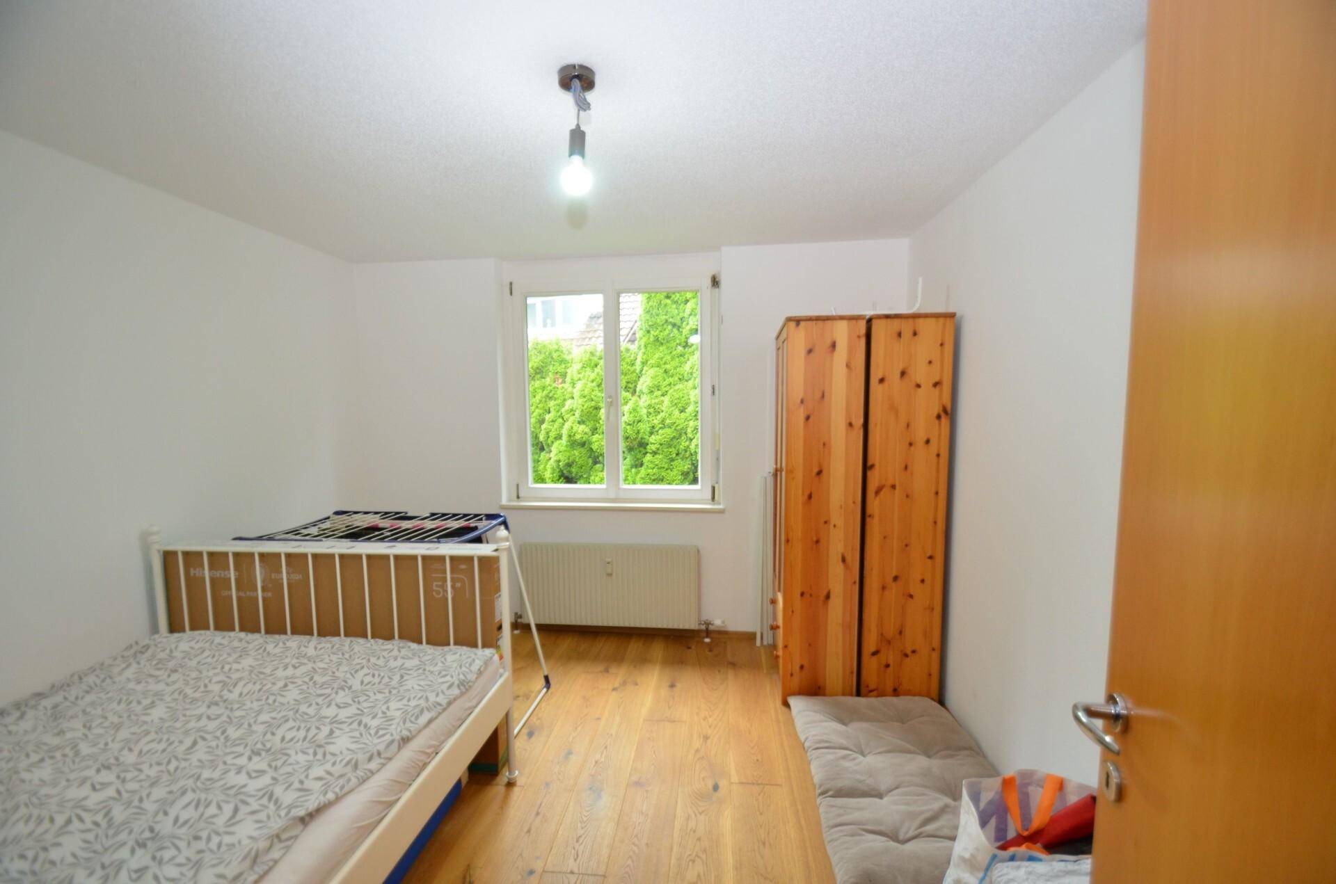 Schlafzimmer mit Holzboden, Einzelbett und Fenster mit Blick ins Grüne.