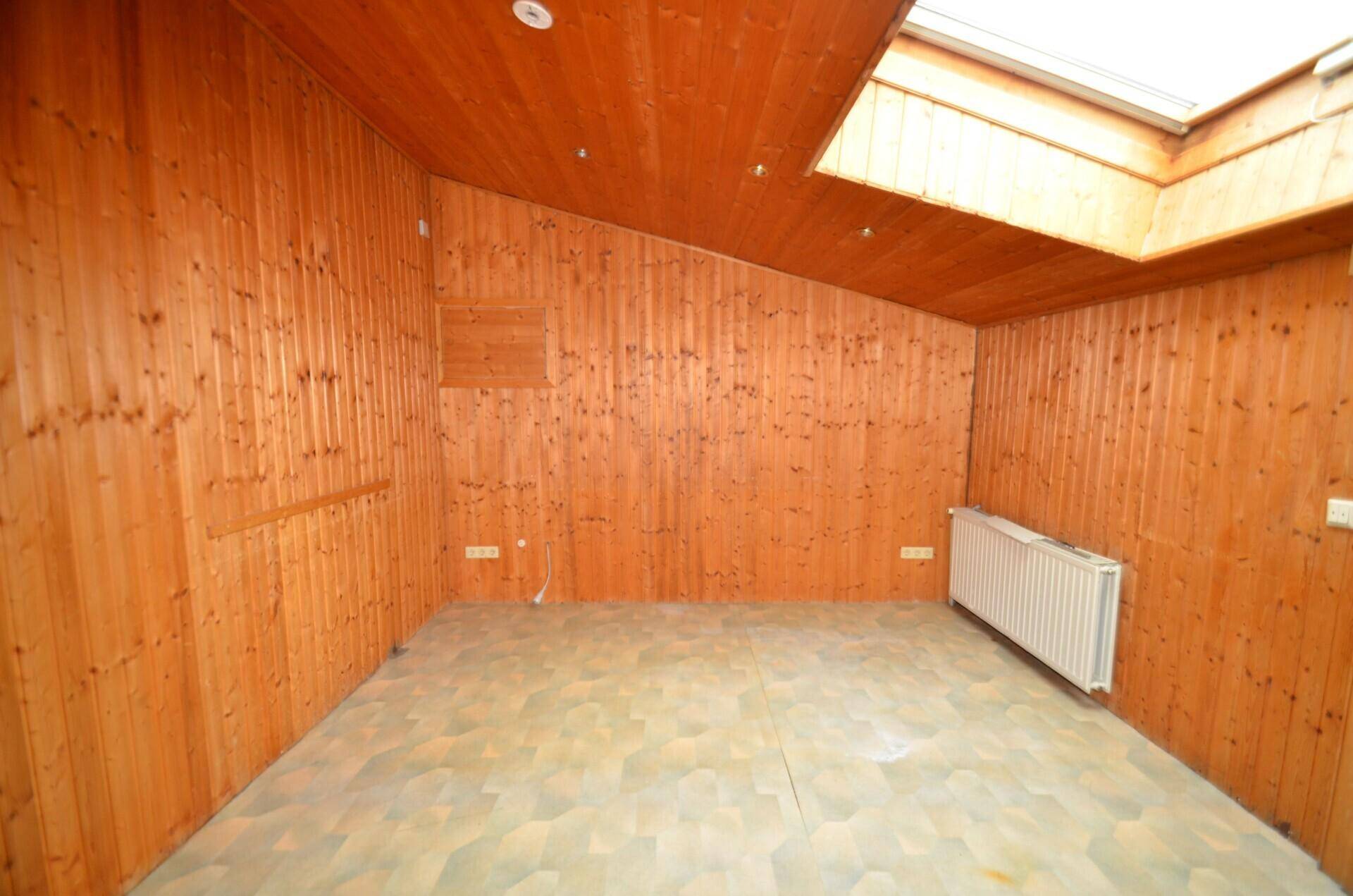Heller Raum mit Holzvertäfelung, Linoleumboden, Dachfenster und Heizkörper, ideal als Schlaf- oder Arbeitszimmer.