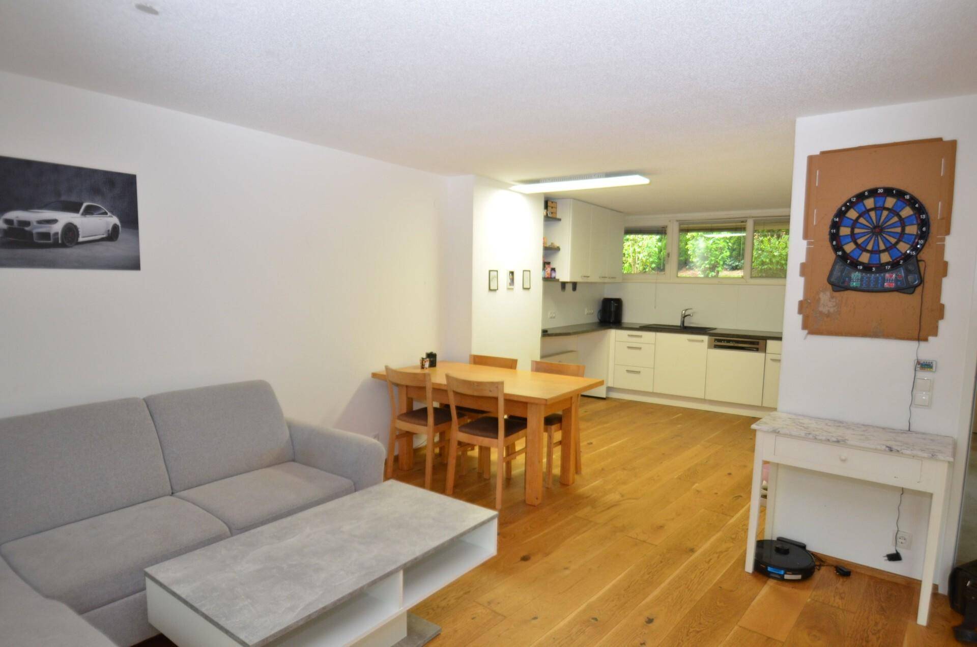Offener Wohn- und Essbereich mit Holzboden, Sofa und integrierter Küche im Hintergrund.