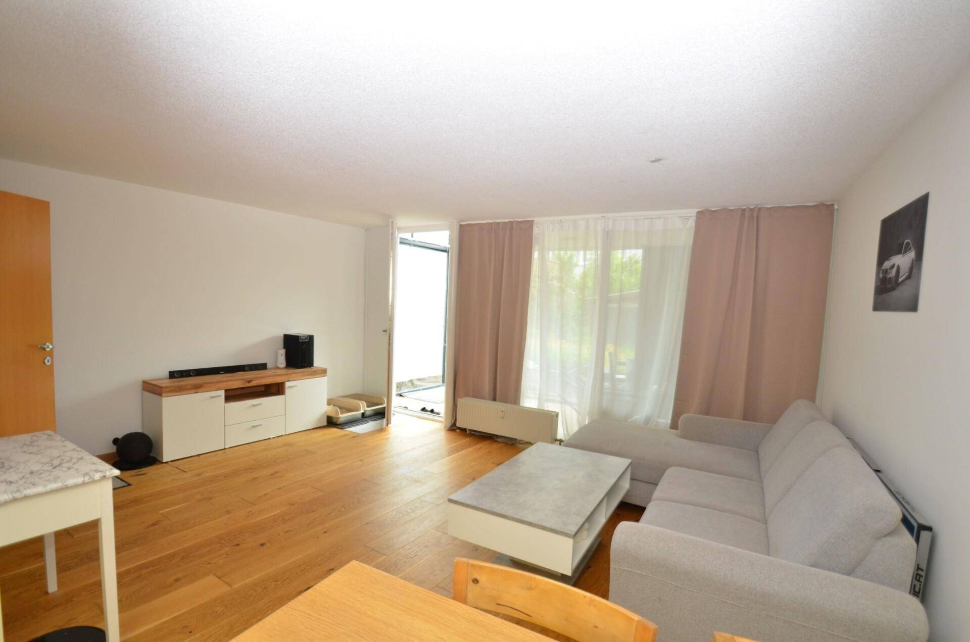 Wohnbereich mit Holzboden, beigem Sofa und einem Medienmöbel, mit Blick auf den Garten.