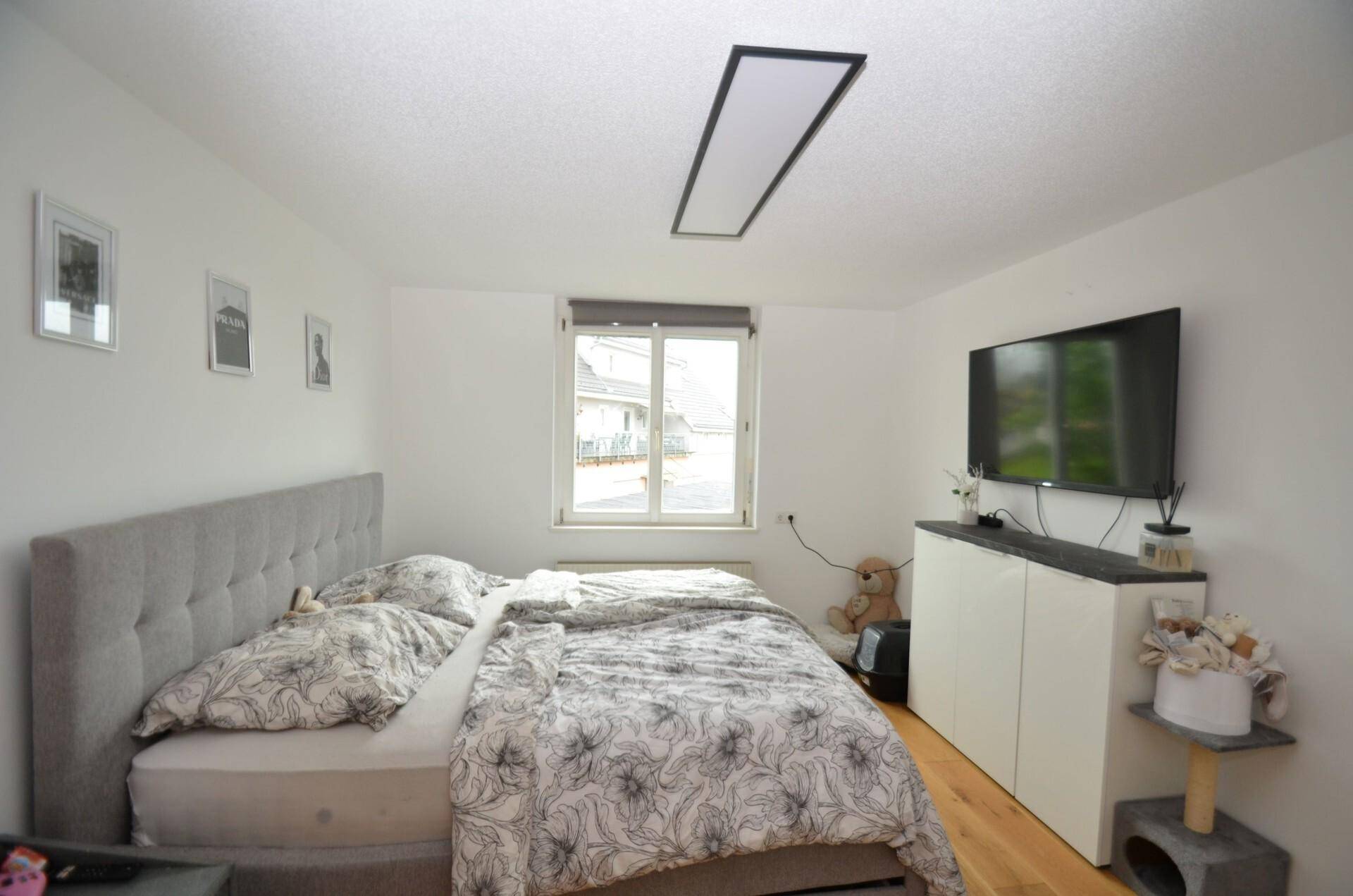 Gemütliches Schlafzimmer mit Doppelbett, Holzboden und Fernseher an der Wand.