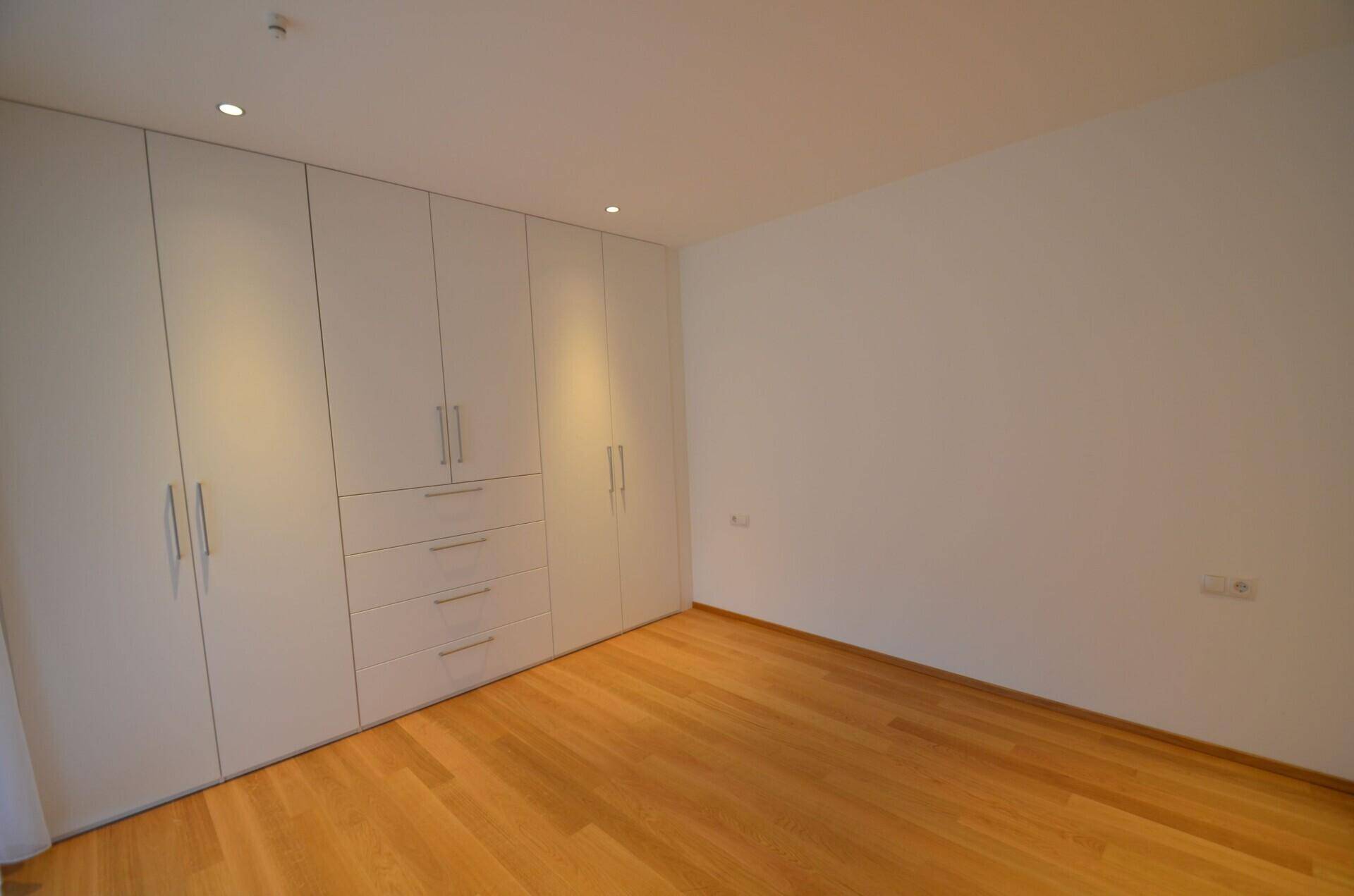 Geräumiges Schlafzimmer mit Holzboden und einer langen Reihe weißer Einbauschränke.