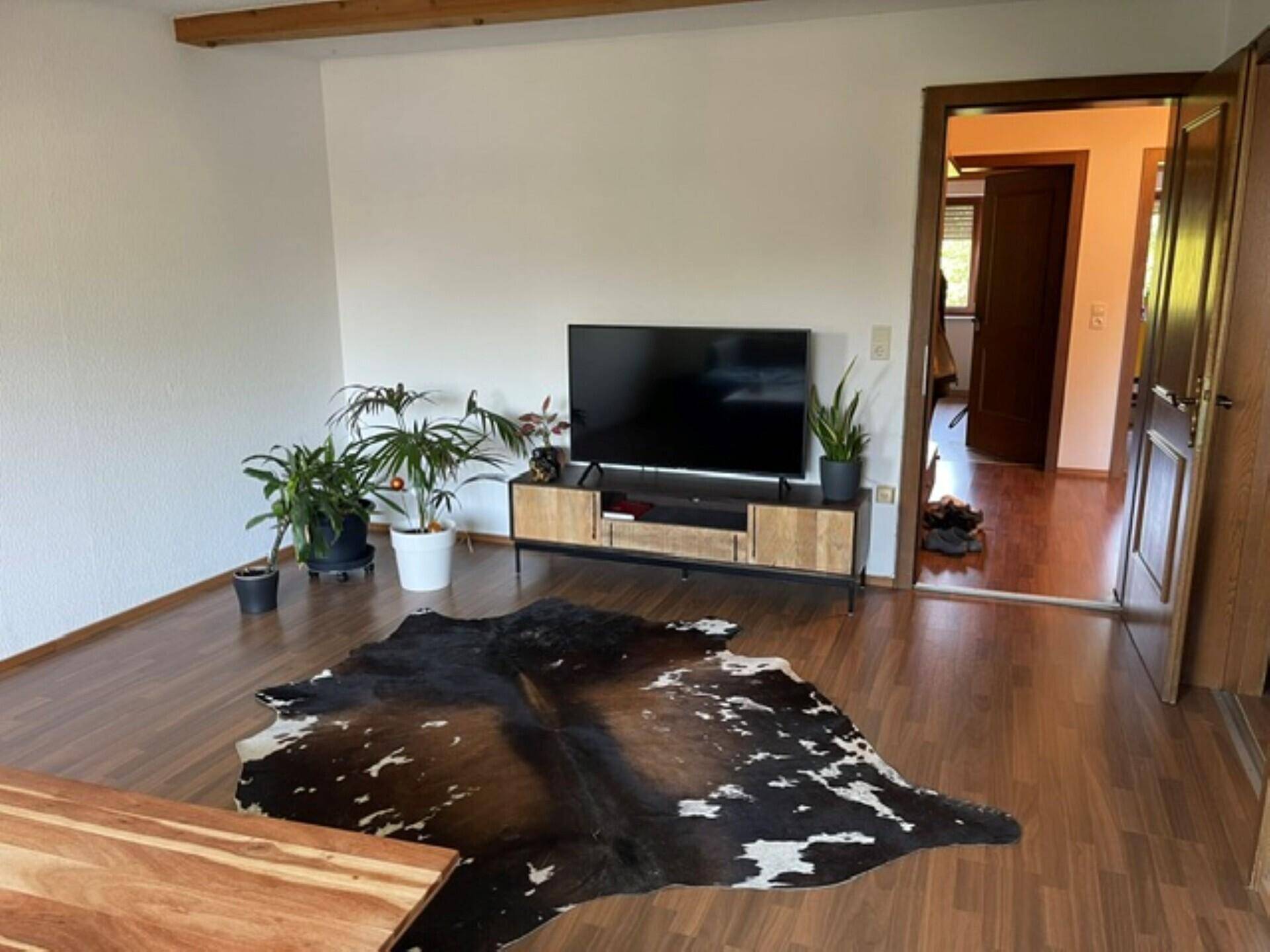 Gemütliches Wohnzimmer mit Holzbalken, Laminatboden und modernem TV-Möbel.