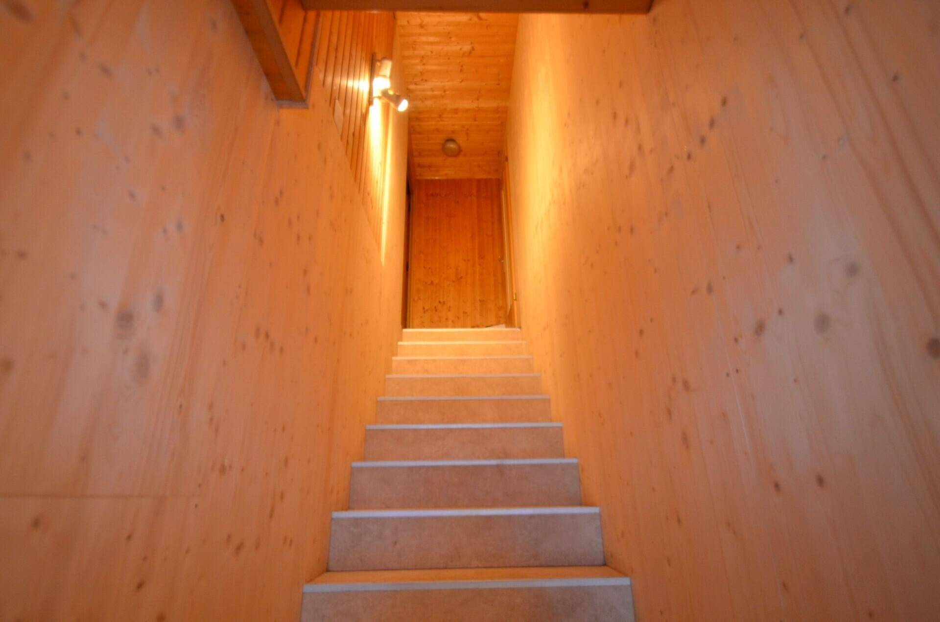Schmaler Treppenaufgang mit Holzvertäfelung an den Wänden und Decke, der zu einem oberen Bereich führt.