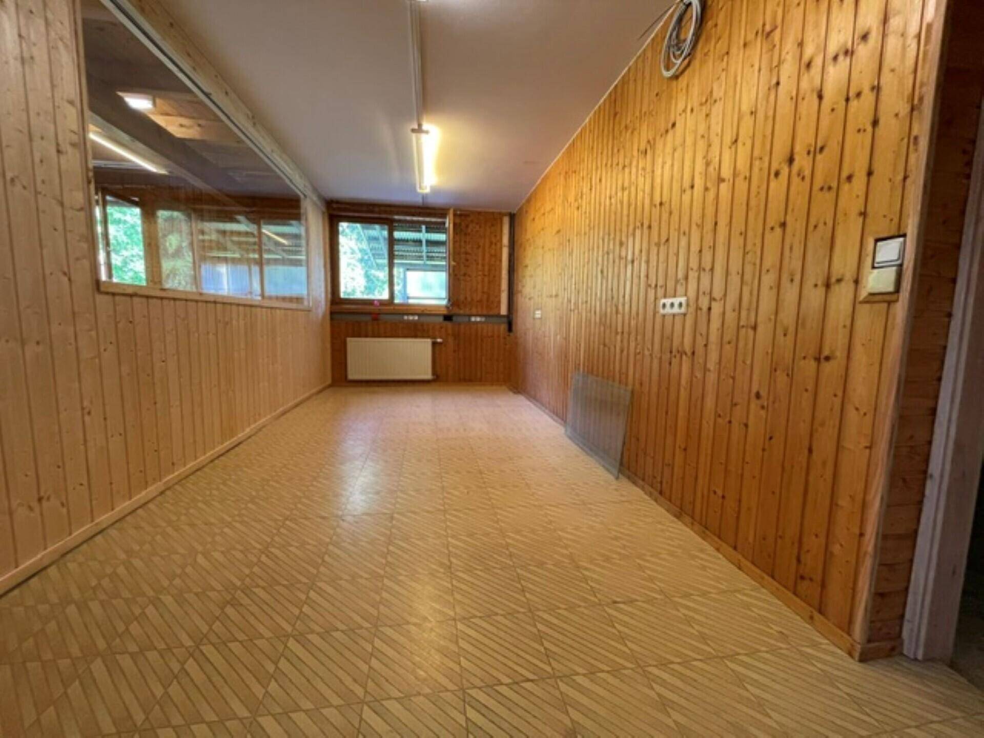 Langer Innenraum mit Holzvertäfelung, Fenstern und einem hellen, gemusterten Bodenbelag.
