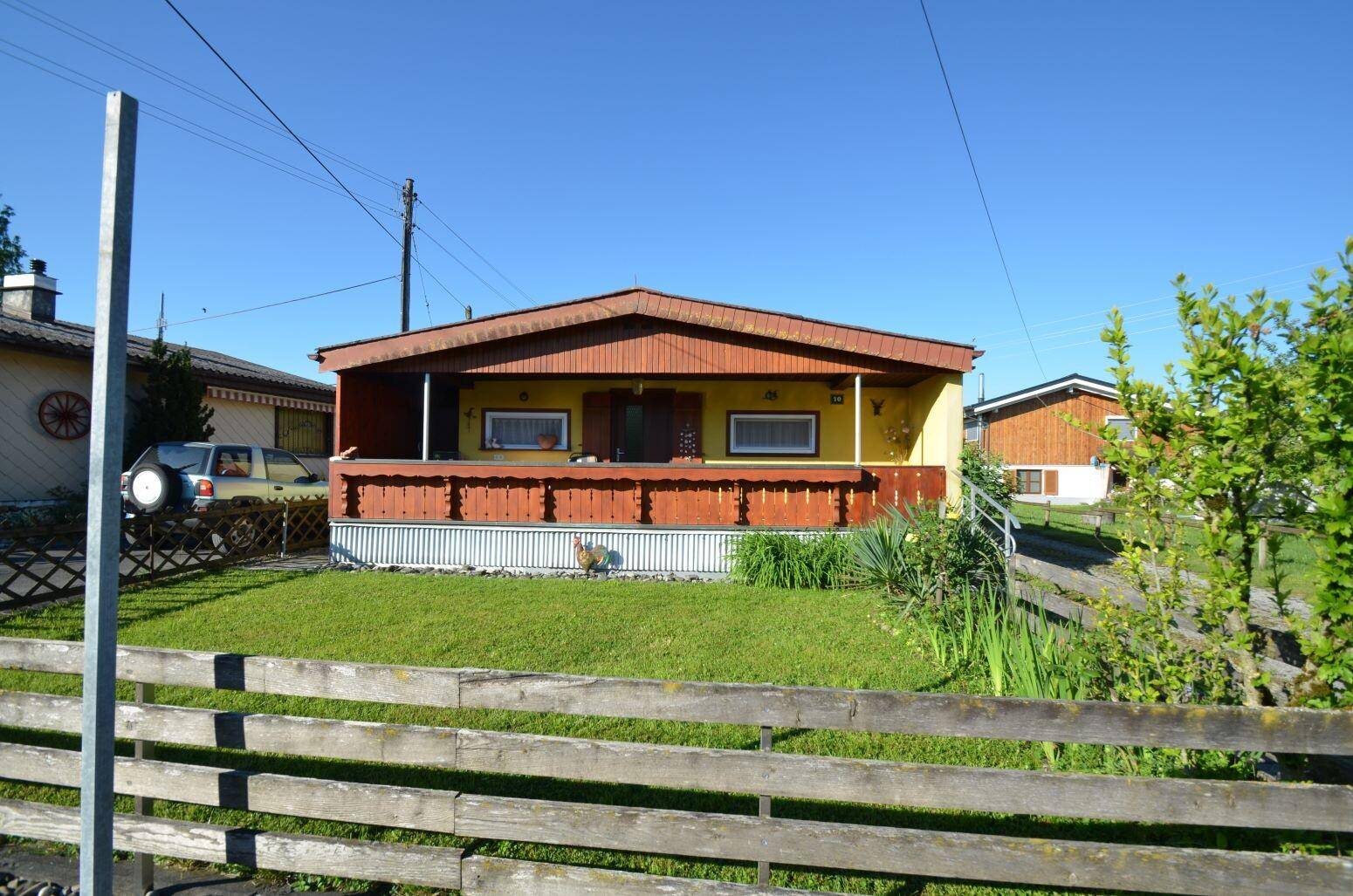 Kleines gelbes Haus mit überdachter Veranda und grünem Vorgarten unter blauem Himmel.