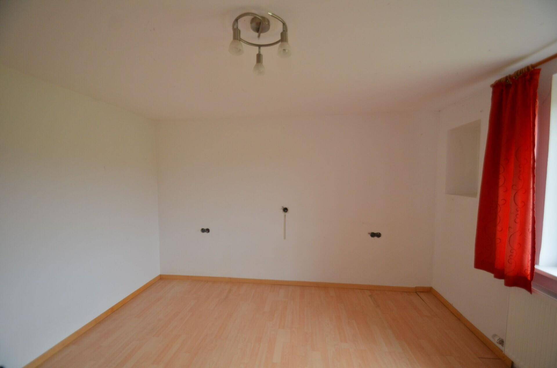 Leerer Raum mit hellem Laminatboden und Anschlüssen an der Wand.