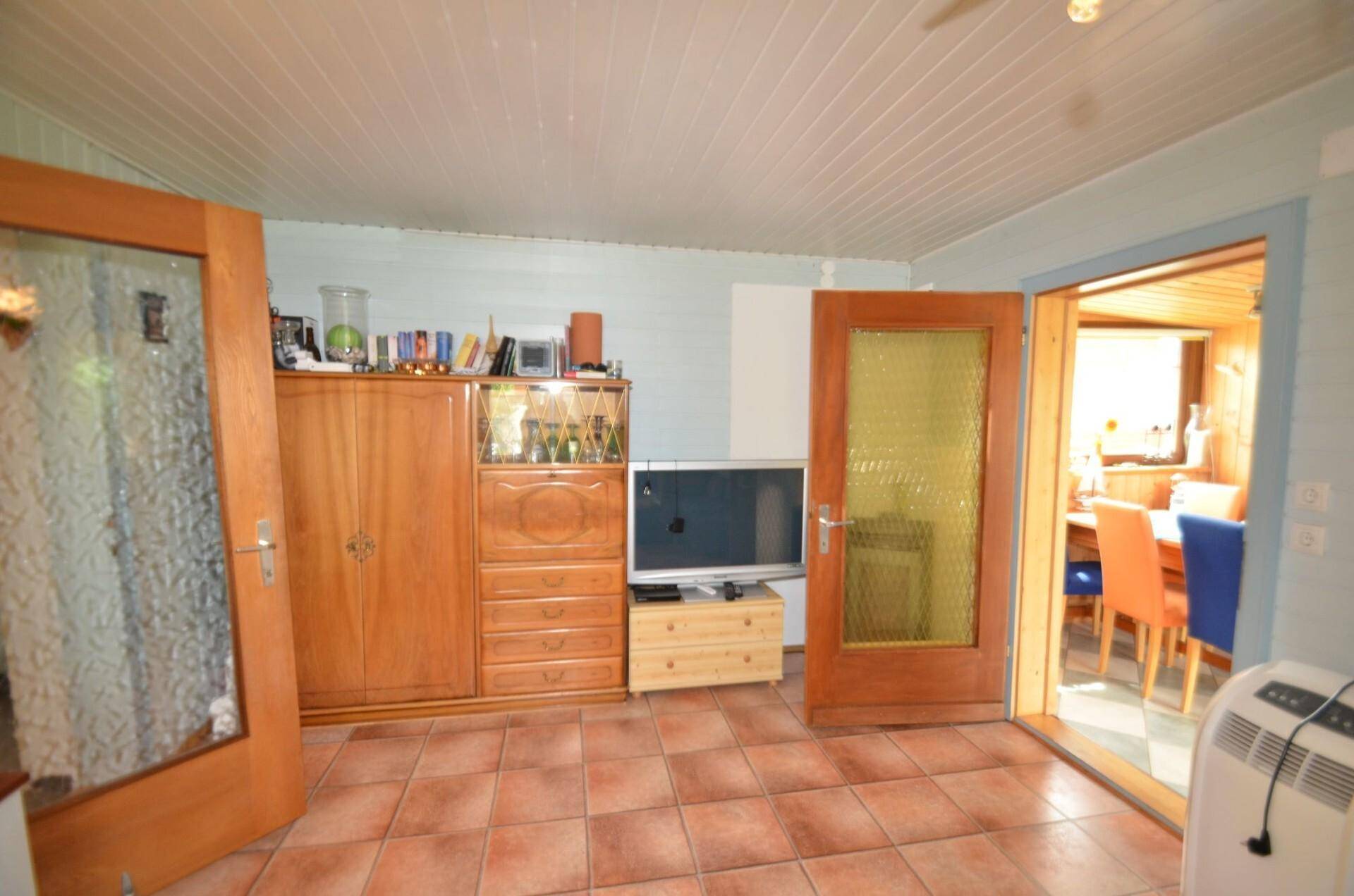 Wohnzimmer mit Terrakottafliesen, Holzmöbeln und einem offenen Zugang zum Essbereich.