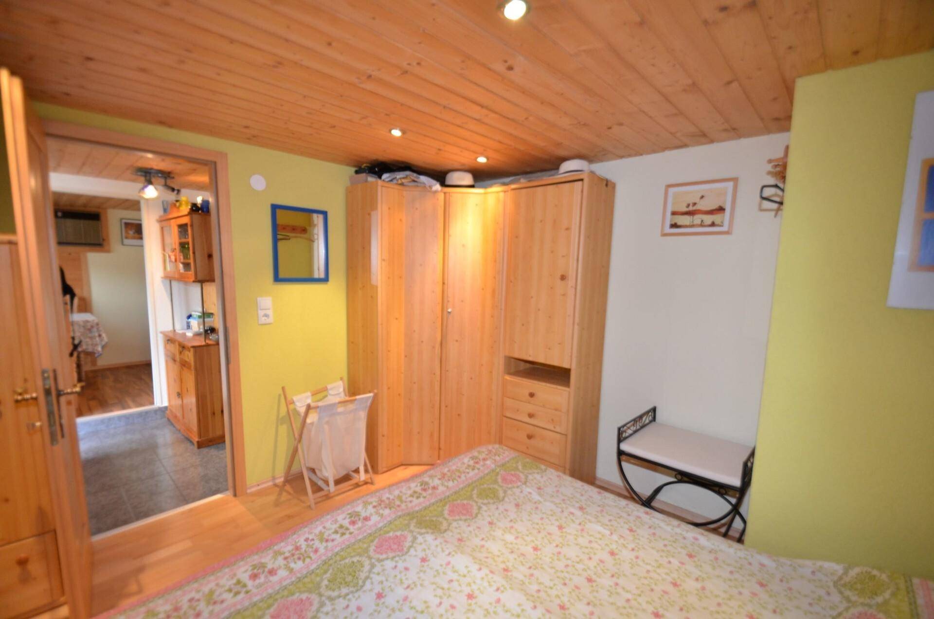 Gemütliches Schlafzimmer mit Holzdecke, Laminatboden und einem großen Eckkleiderschrank.