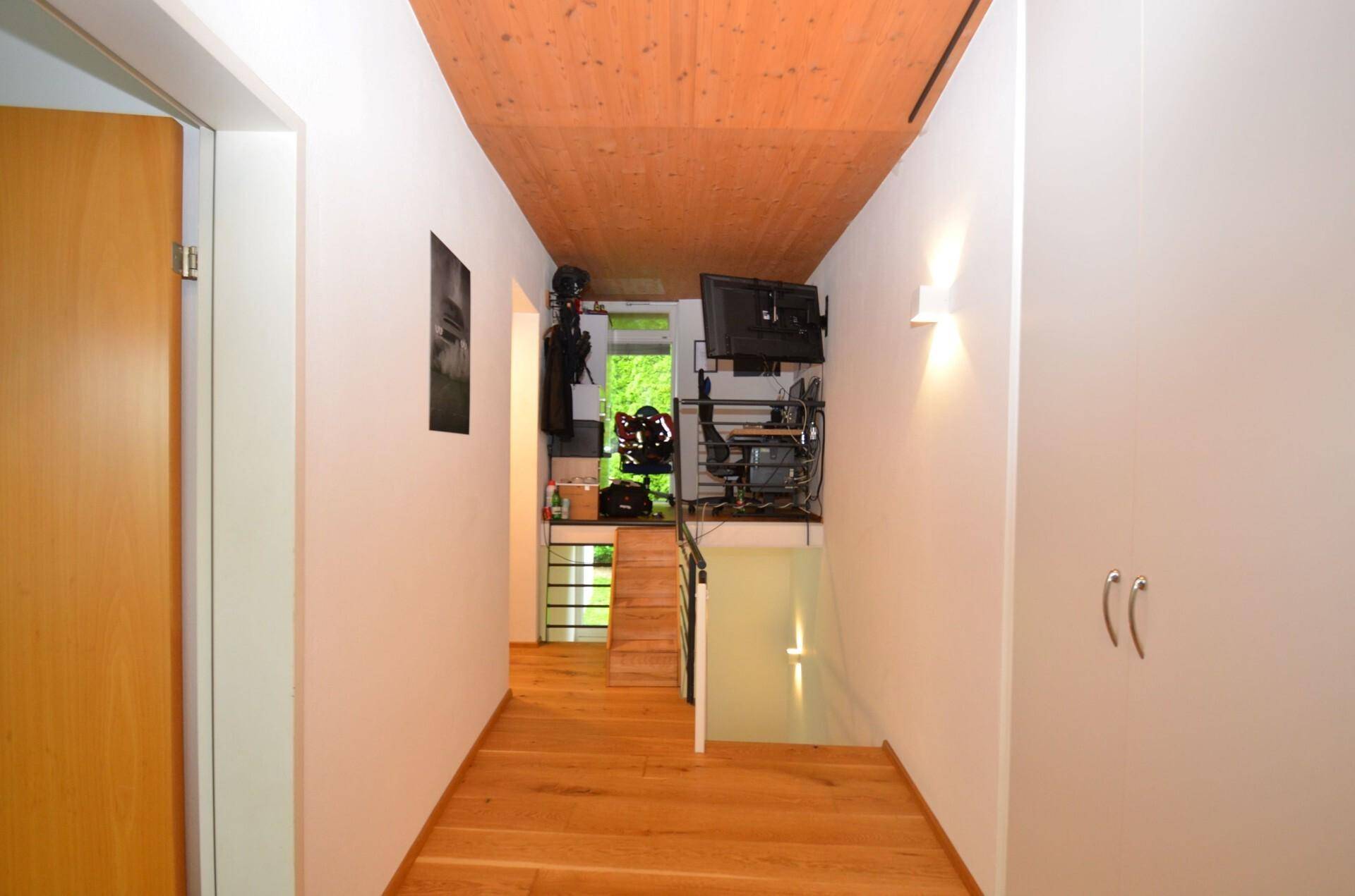 Langer Flur mit Holzboden und Holzdecke, der zu einem Arbeitsbereich führt.