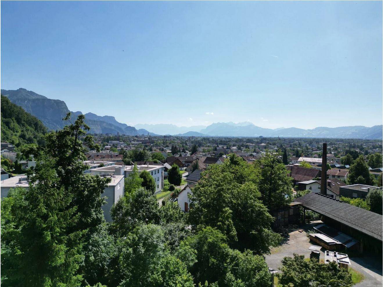 Panoramablick über die Stadtlandschaft mit üppigem Grün und einer beeindruckenden Bergkulisse.
