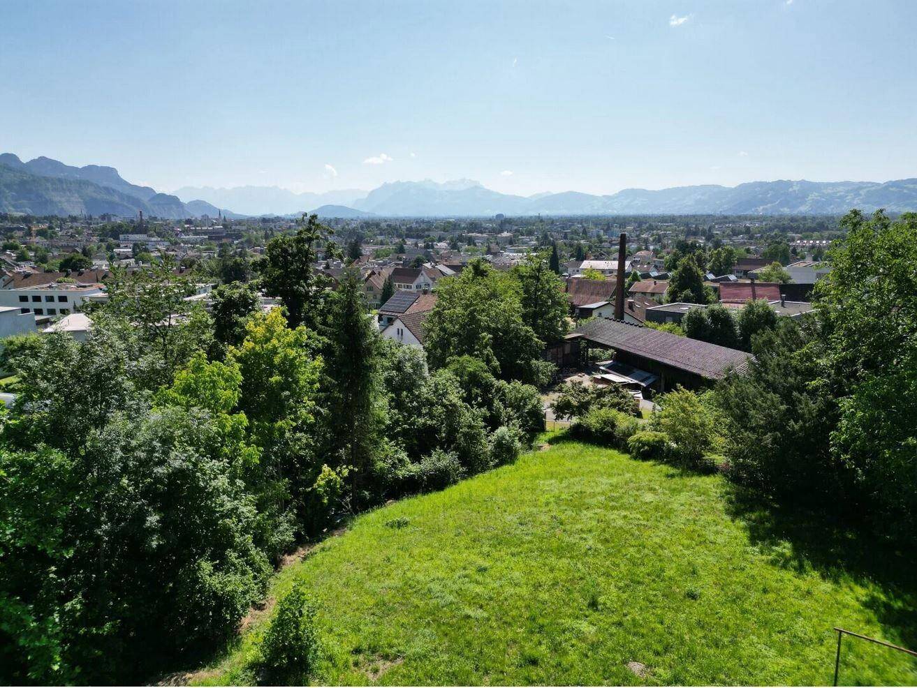 Umfassender Blick auf die Stadt mit vielen Bäumen und einer malerischen Bergkette am Horizont.