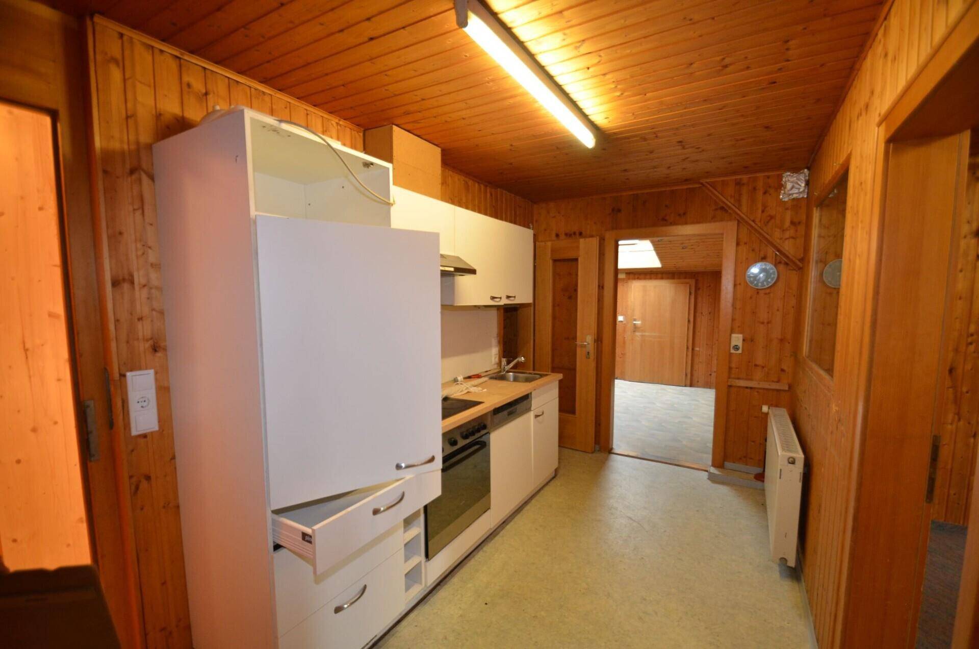 Kleine, funktionale Küche mit weißen Schränken, Spüle und Kochfeld, integriert in einen Raum mit Holzvertäfelung.