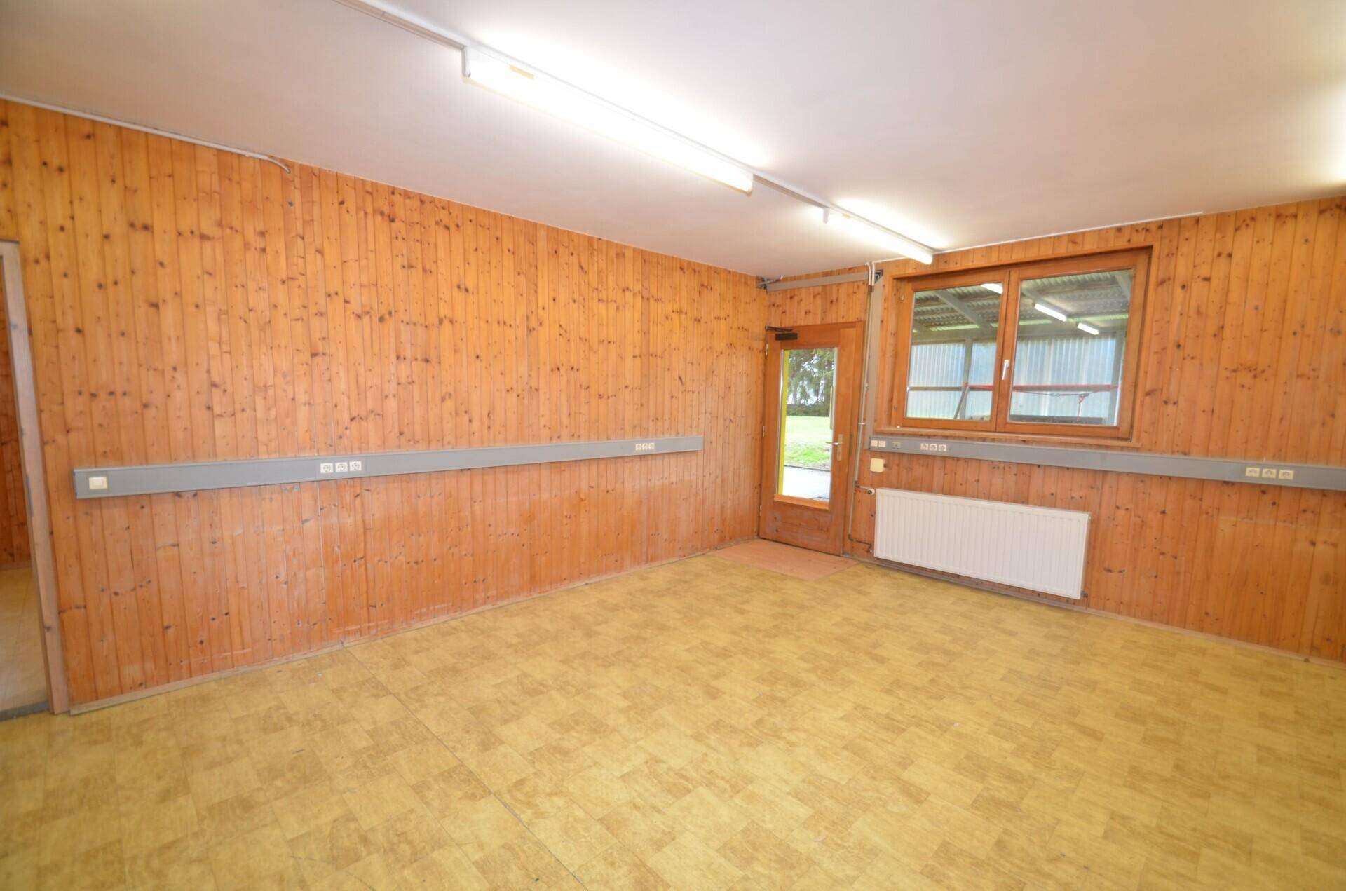 Heller Raum mit Holzvertäfelung, Linoleumboden und einer Tür, die ins Freie führt, sowie einem Fenster.