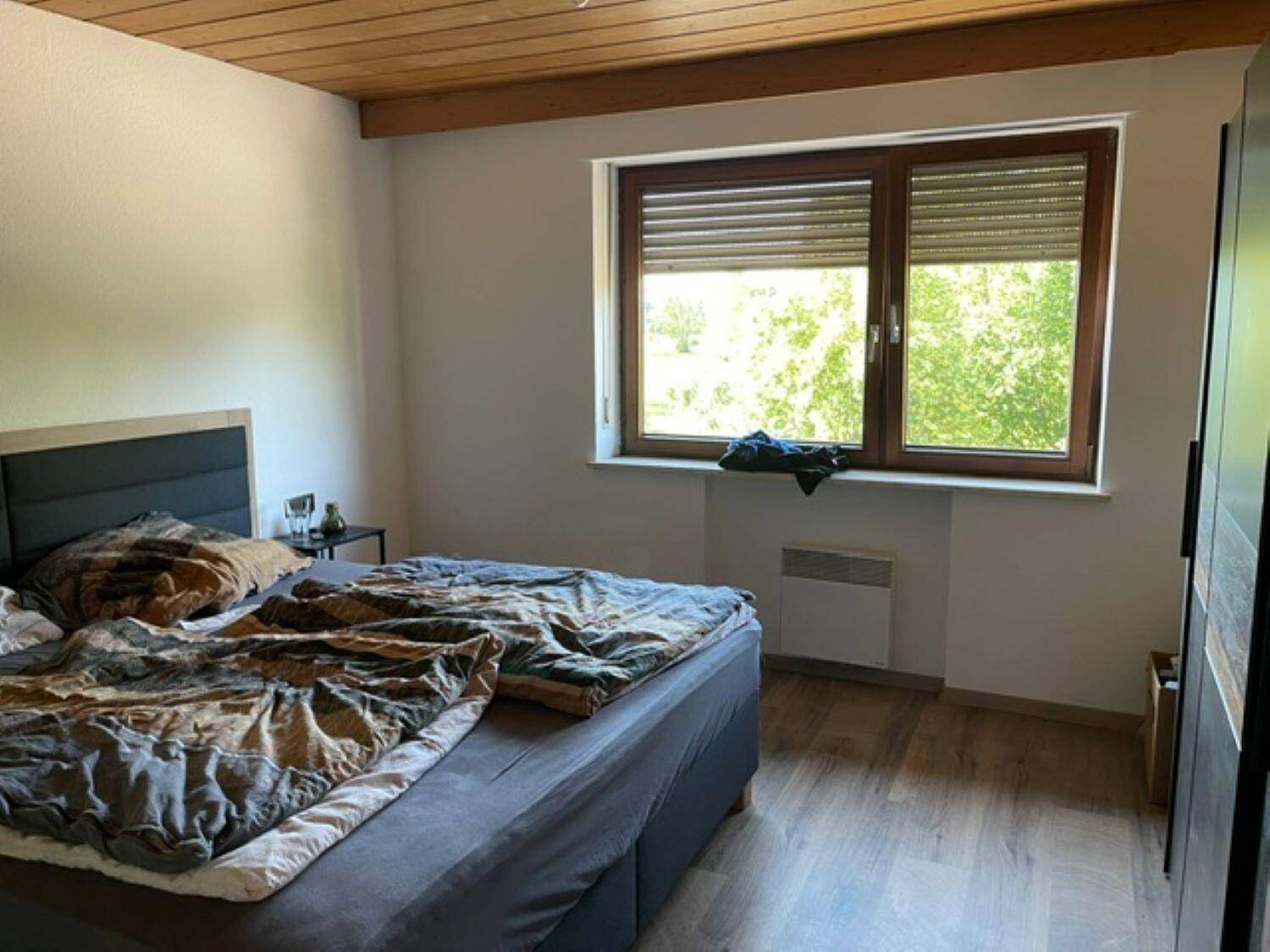 Schlafzimmer mit Doppelbett, Laminatboden und Fenster mit Rollläden und Blick ins Grüne.