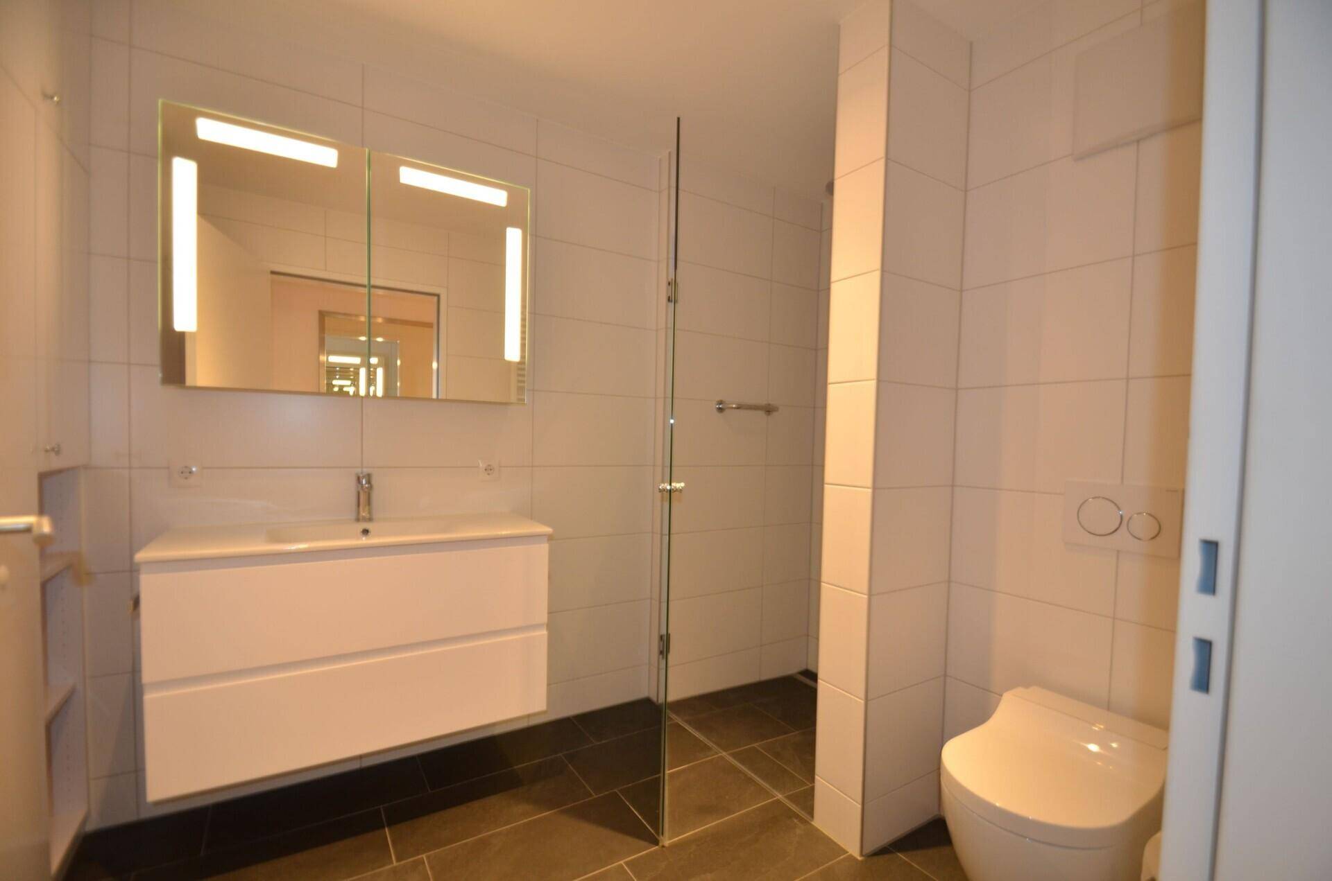 Modernes Badezimmer mit weißen Wandfliesen, dunklem Boden und einer begehbaren Dusche.