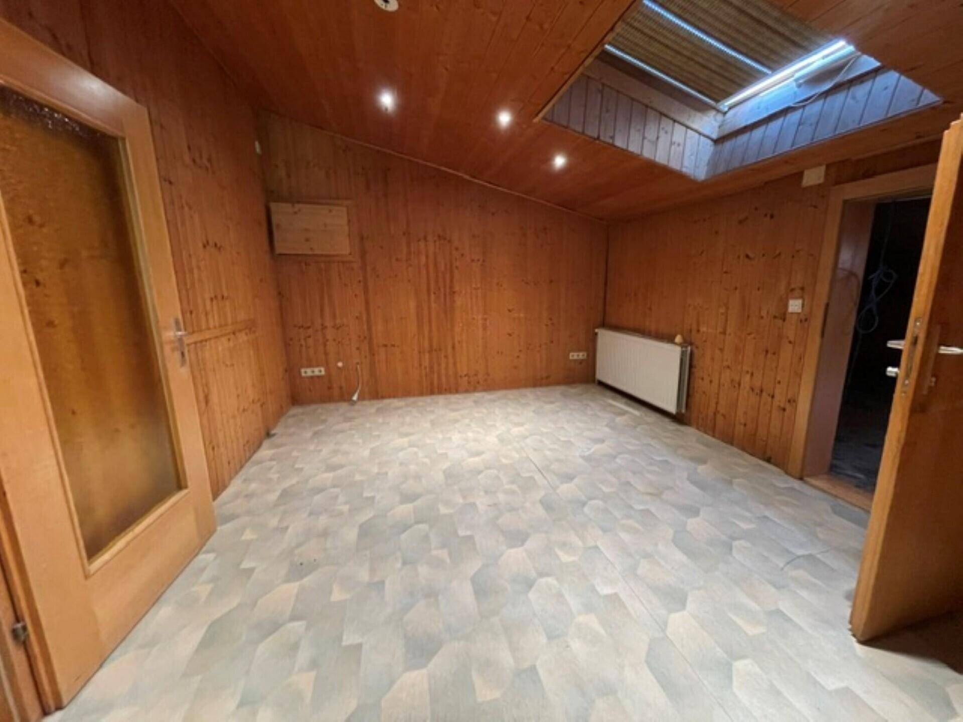Innenraum mit Holzvertäfelung, Dachschräge, Oberlicht, Einbaustrahlern und hellem Bodenbelag.