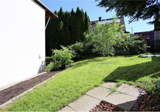 Gepflegter Gartenbereich mit Rasenfläche, Sträuchern und einem Baum, ideal zum Entspannen.