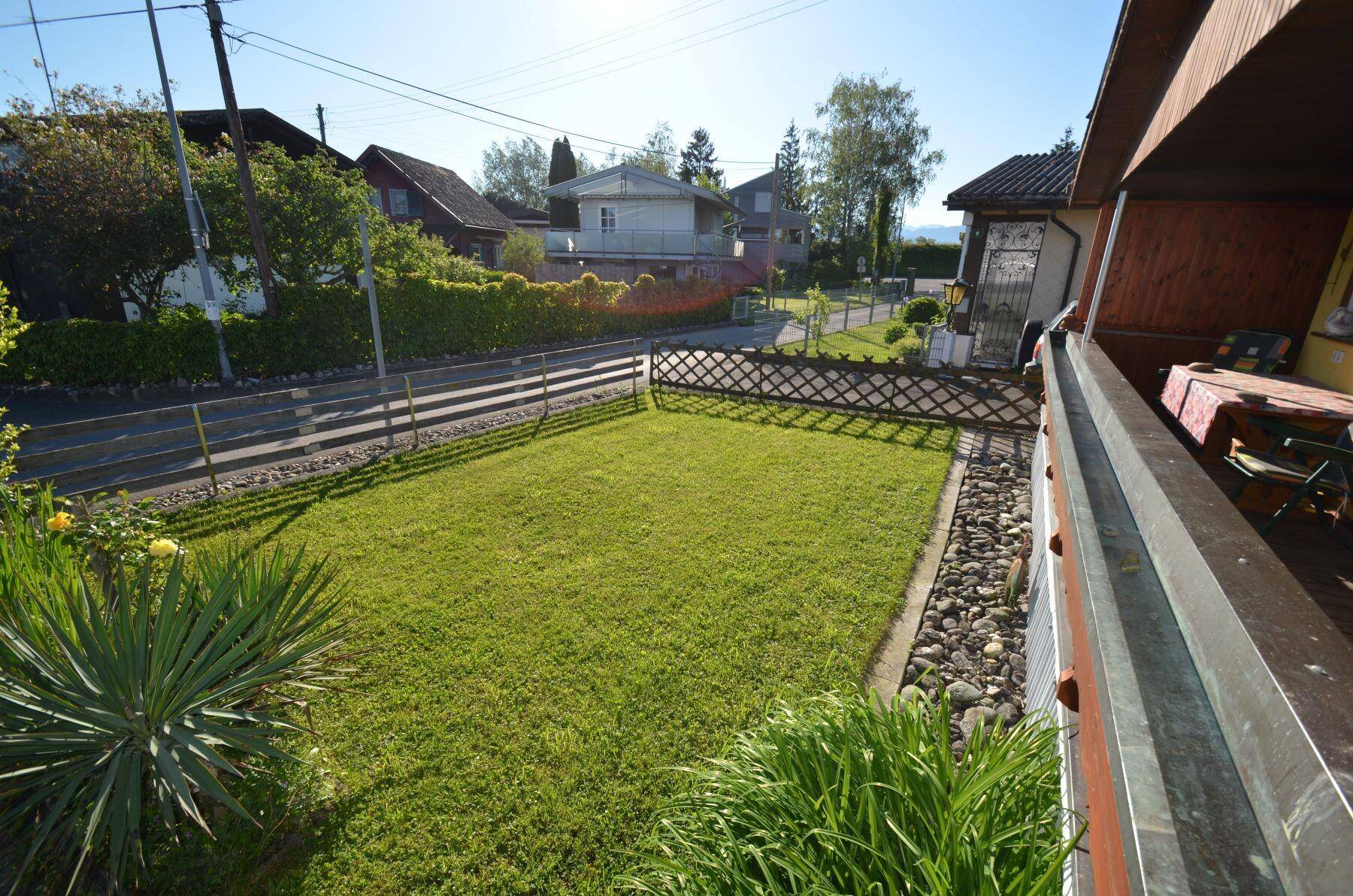 Gepflegter Rasen im Vorgarten, gesehen vom überdachten Balkon, mit Blick auf die Straße.