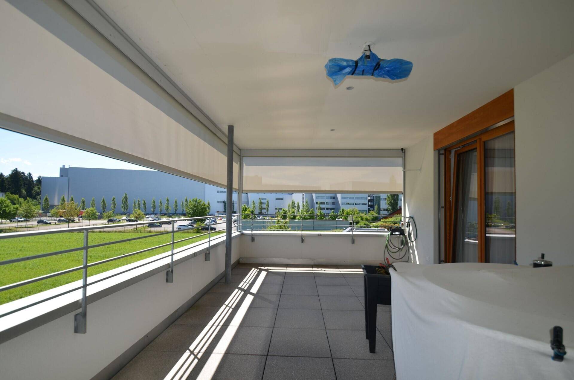 Geräumiger Balkon mit Fliesenboden und Blick auf die umliegende Industrie und Grünflächen.