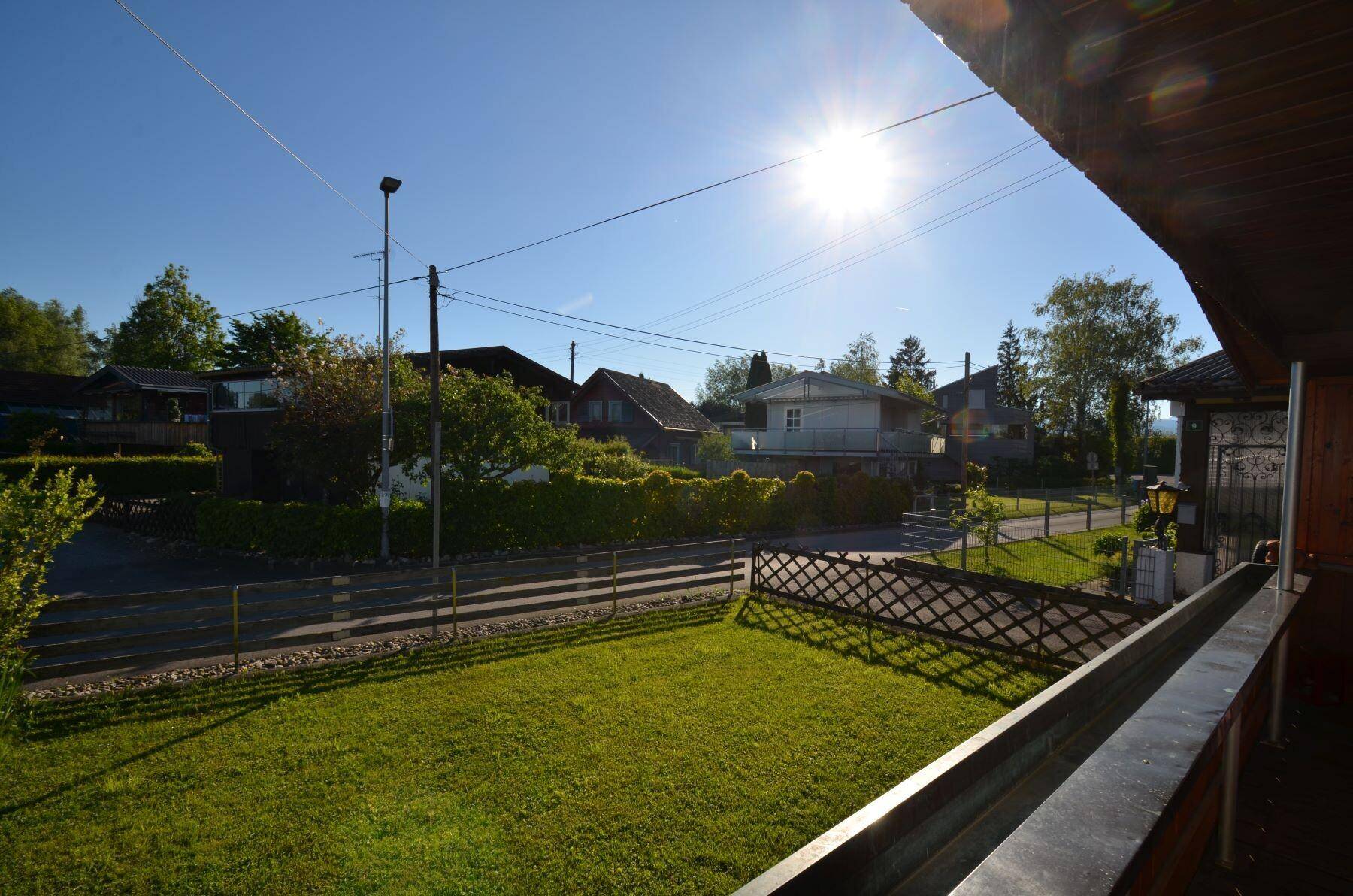 Sonniger Ausblick vom überdachten Balkon auf den Garten und die umliegende Wohngegend.