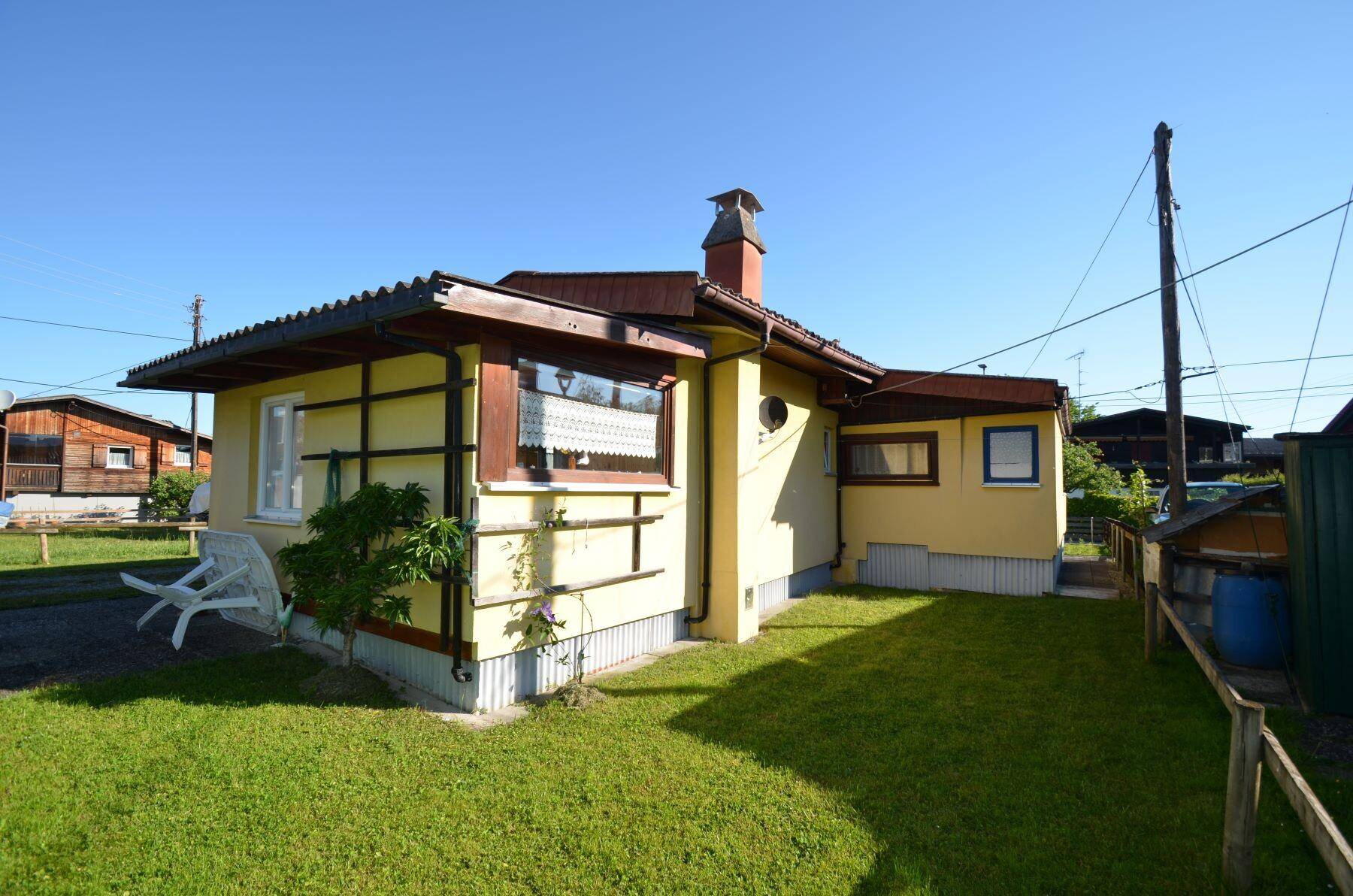 Seitenansicht des Hauses mit gelber Fassade, kleinem Rasenbereich und Schornstein.
