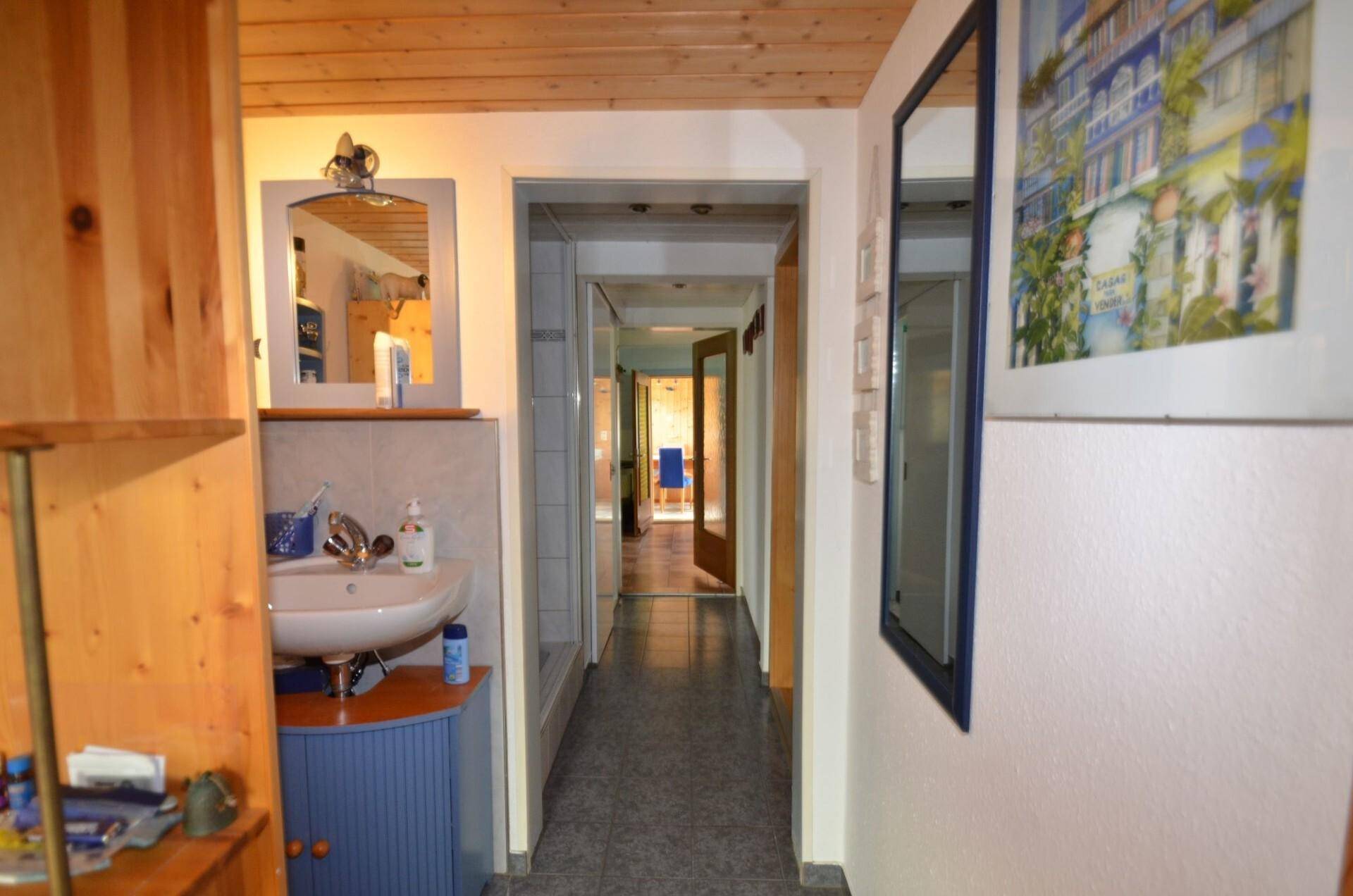 Flur mit Holzdecke, kleinem Waschbecken und Spiegel, der zu weiteren Räumen führt.
