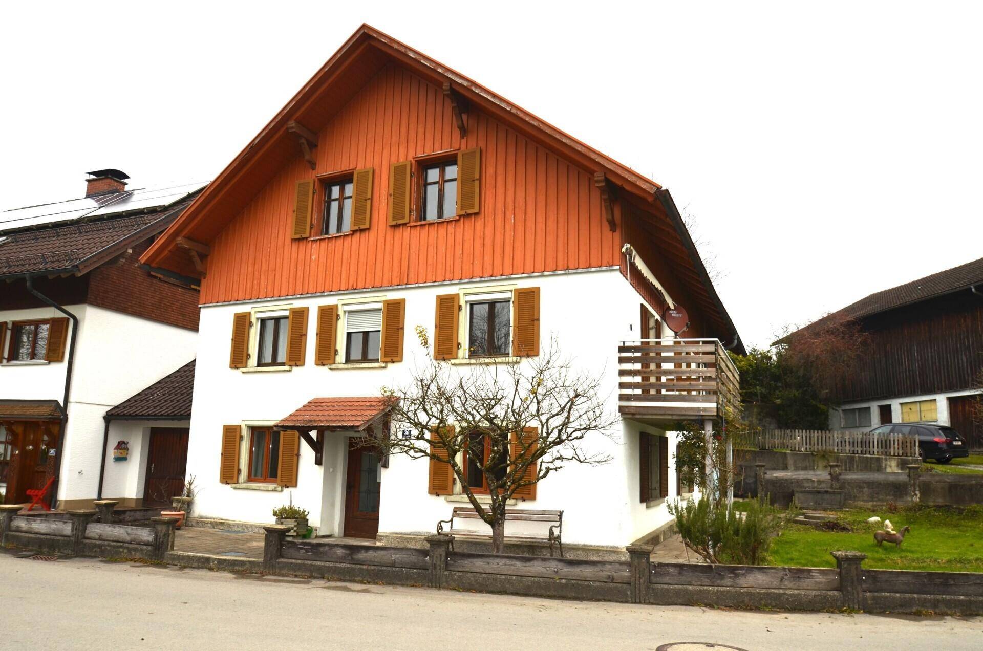 Vorderansicht des Hauses mit Balkon, Holzverkleidung und traditionellen Fensterläden.