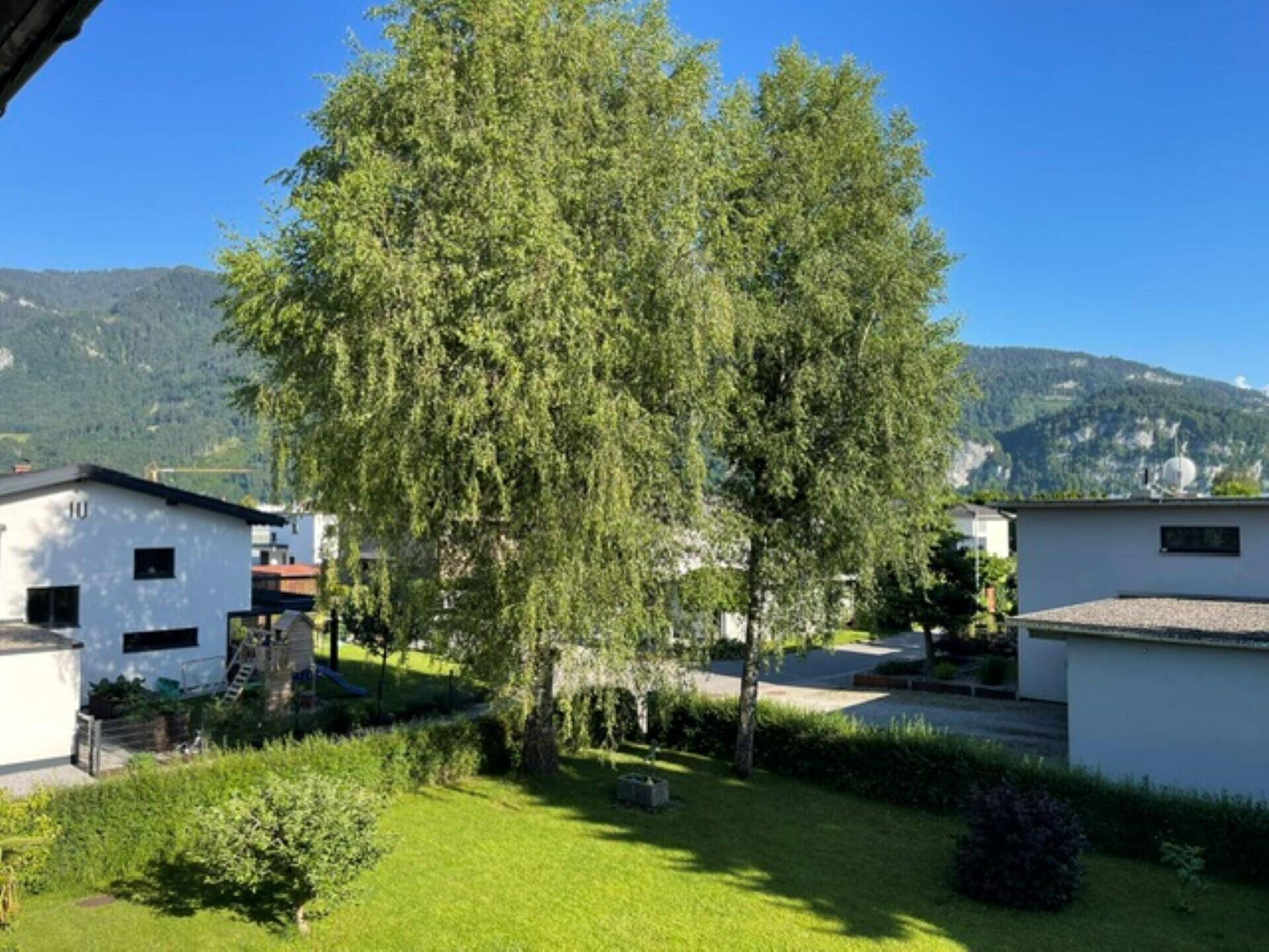Weitläufiger Garten mit großen Bäumen und Blick auf die umliegende Natur und Berge.