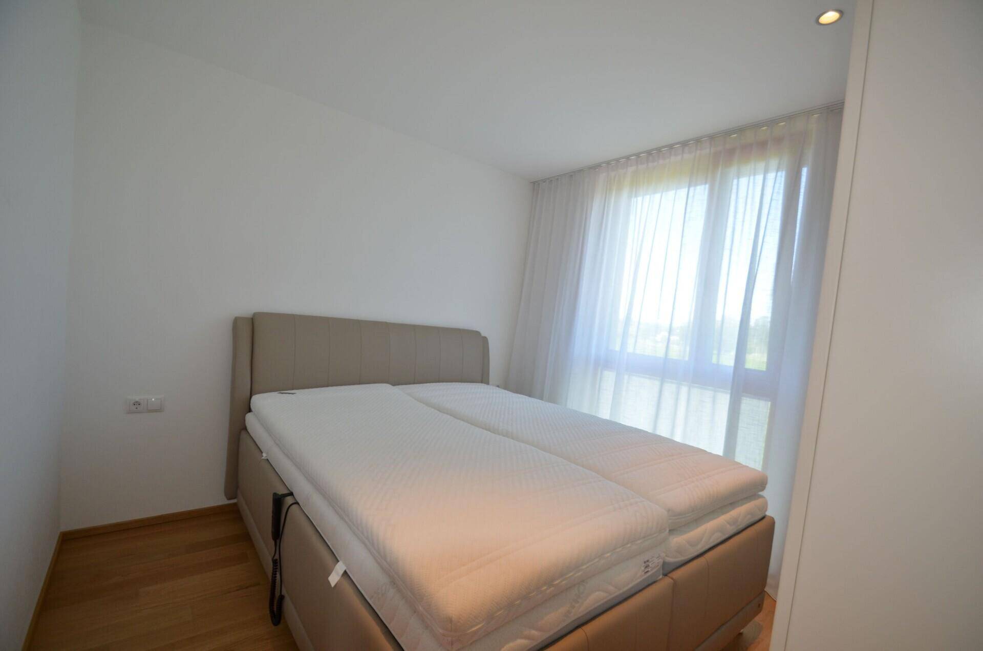 Helles Schlafzimmer mit Doppelbett, Holzboden und viel Tageslicht durch das große Fenster.
