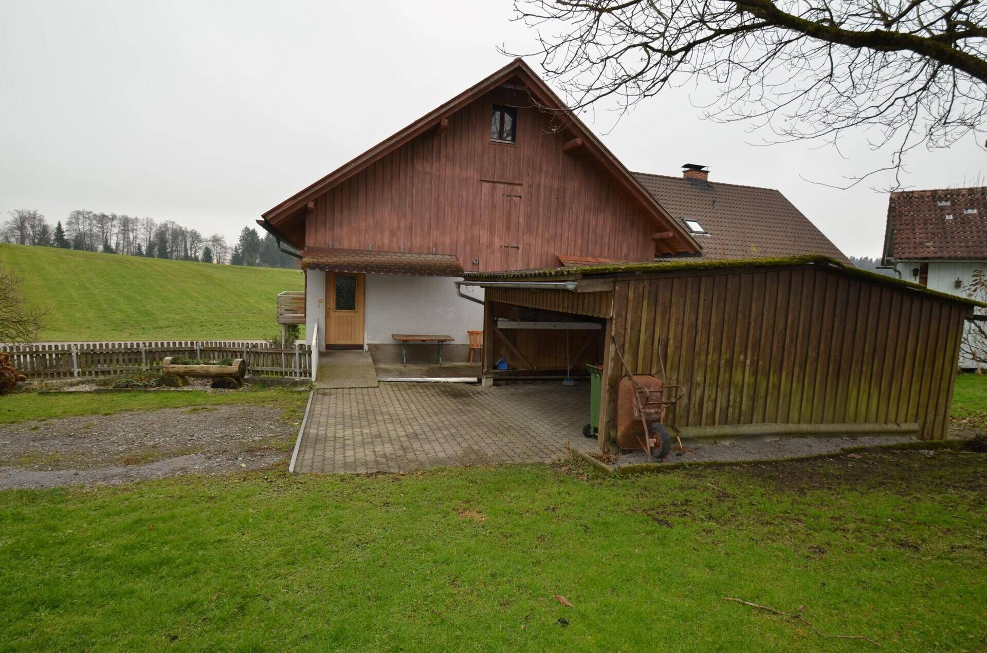 Seitenansicht des Hauses mit Carport, Zufahrt und angrenzendem Gartenbereich.