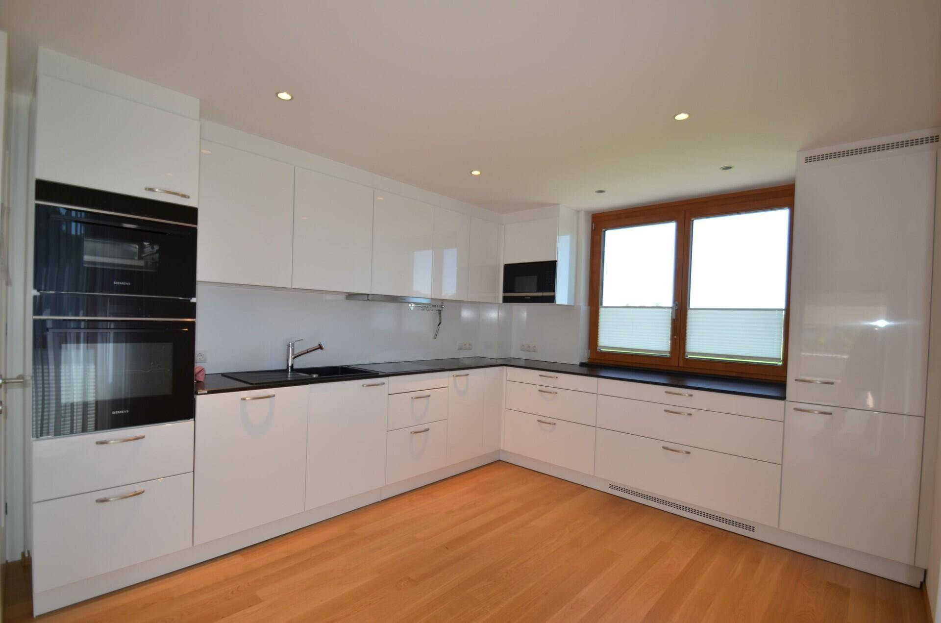Moderne Küche mit weißen Hochglanzfronten, schwarzen Arbeitsplatten und integrierten Geräten.