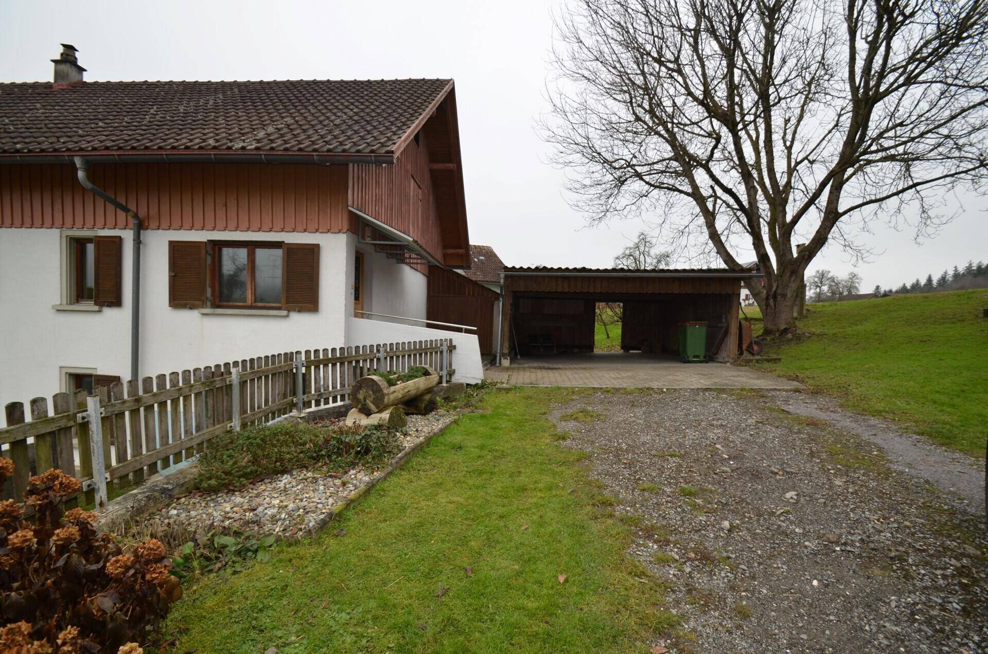 Seitenansicht des Hauses mit Carport, Zufahrt und angrenzendem Gartenbereich.