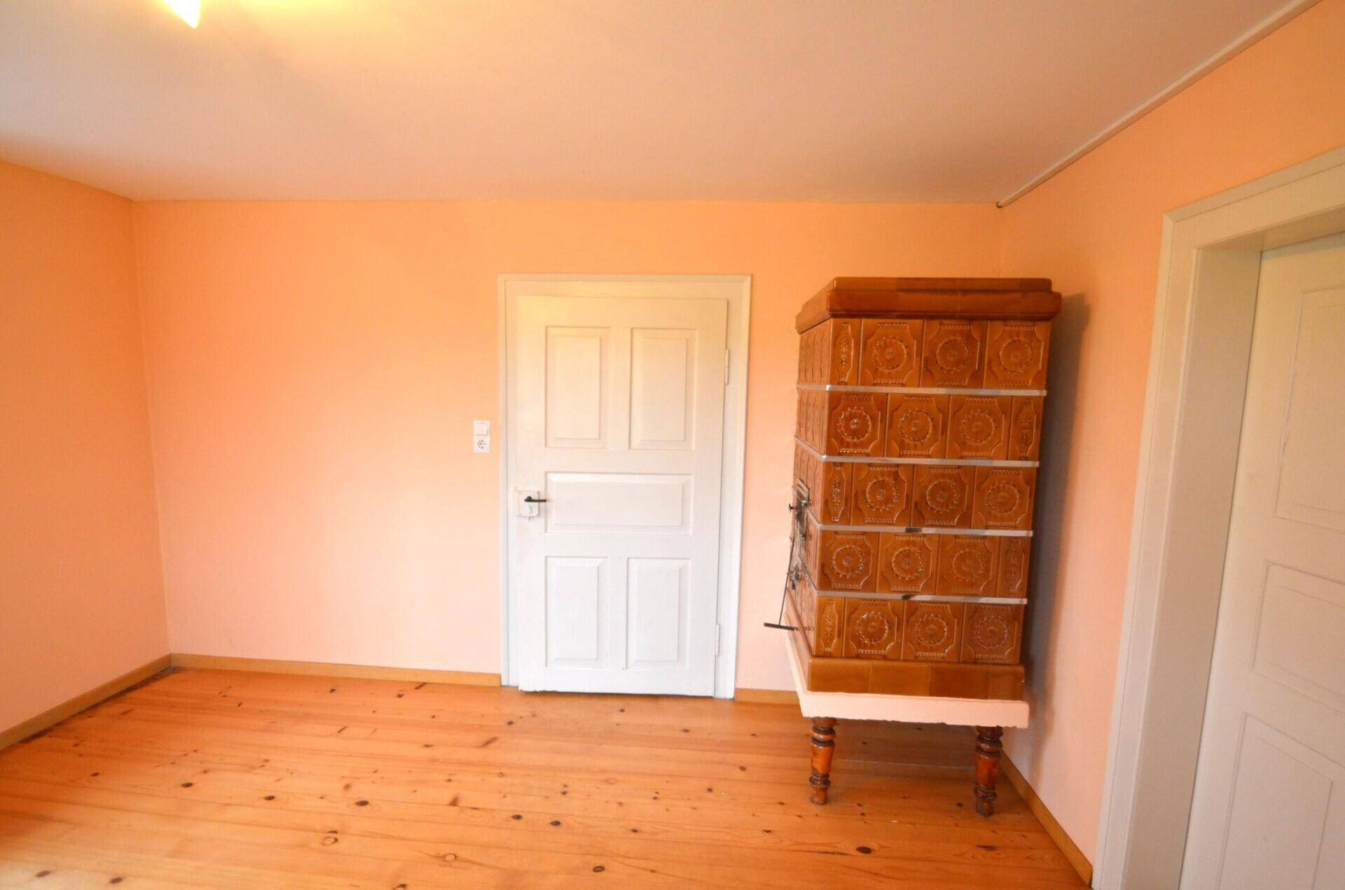 Gemütliches Zimmer mit Holzdielenboden, pastellfarbenen Wänden und einem Kachelofen.