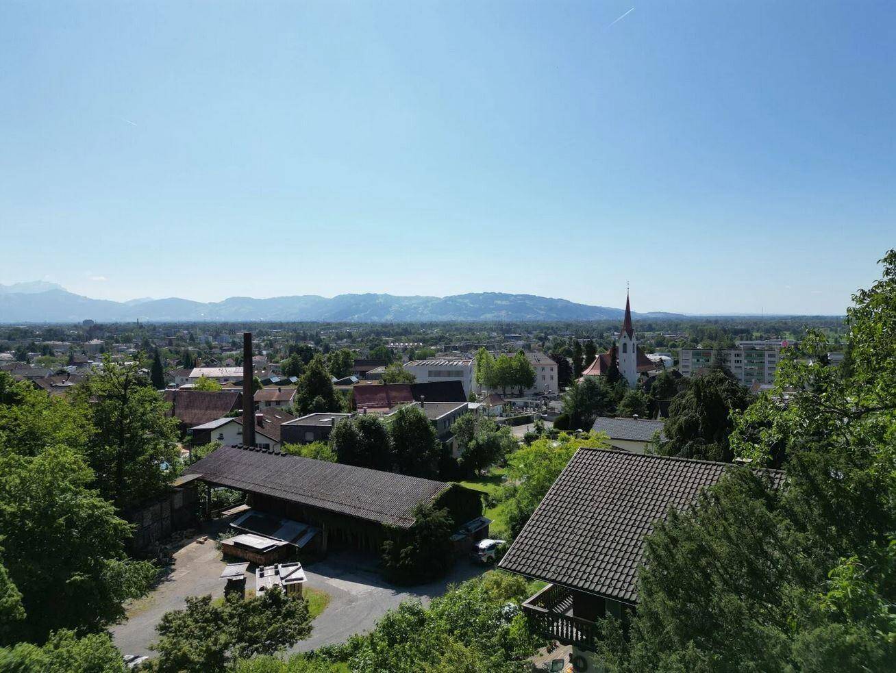 Aussicht über eine charmante Stadt mit Kirchturm, umgeben von grünen Hügeln und Bergen.