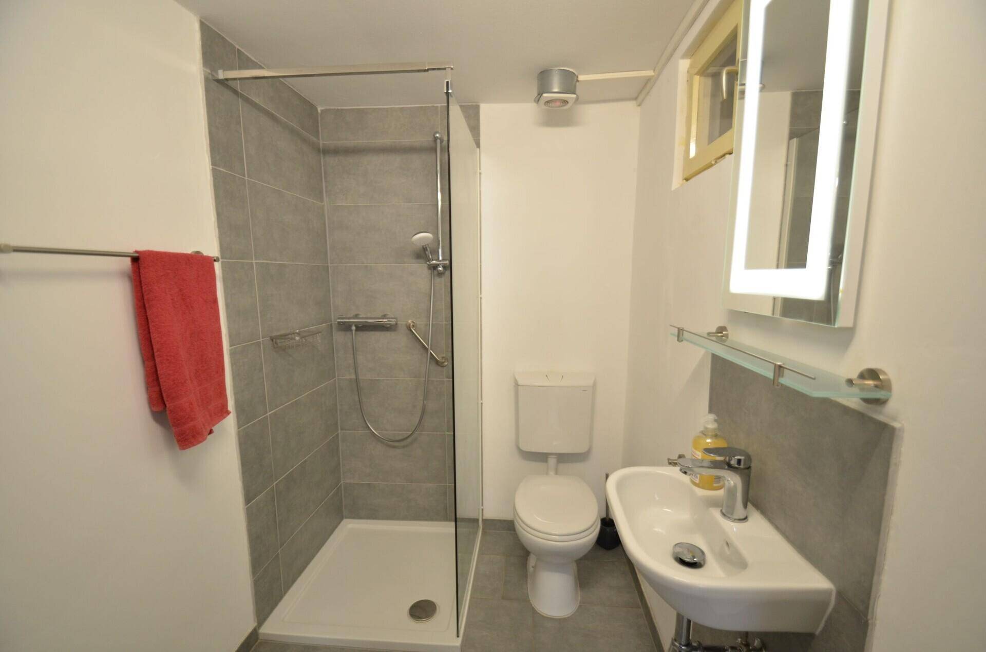 Modernes Badezimmer mit Duschkabine, WC, Waschbecken und beleuchtetem Spiegelschrank.