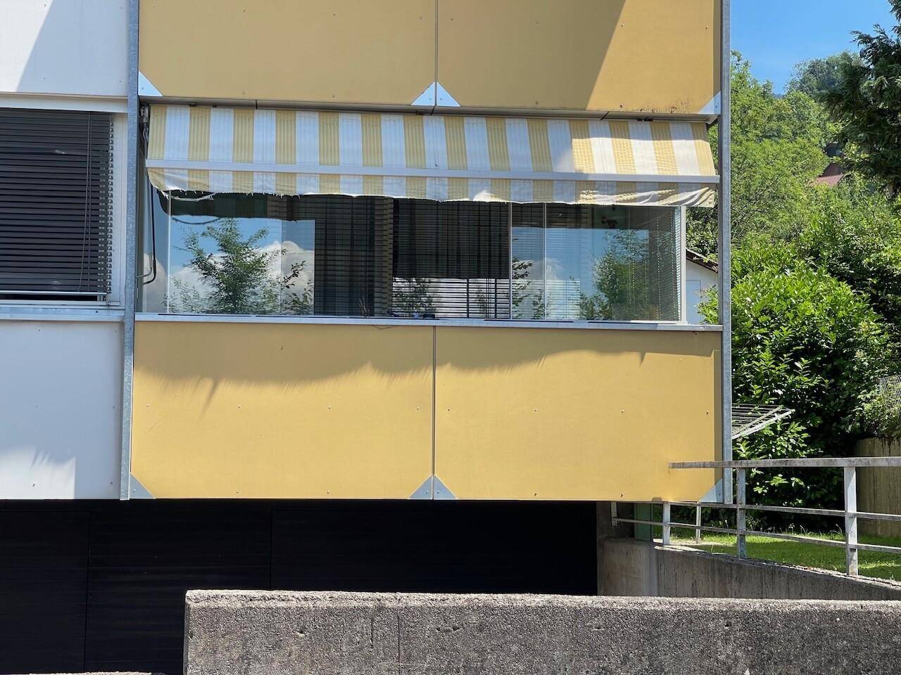 Fenster mit gestreifter Markise an der Gebäudefassade, bietet Schutz vor Sonne und eine Rampe für den Zugang.