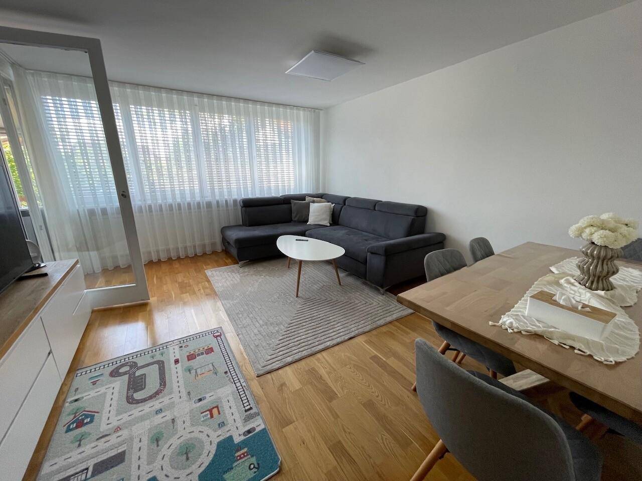 Geräumiger Wohn- und Essbereich mit dunklem Sofa, Esstisch und hellem Holzboden, ideal für geselliges Beisammensein.