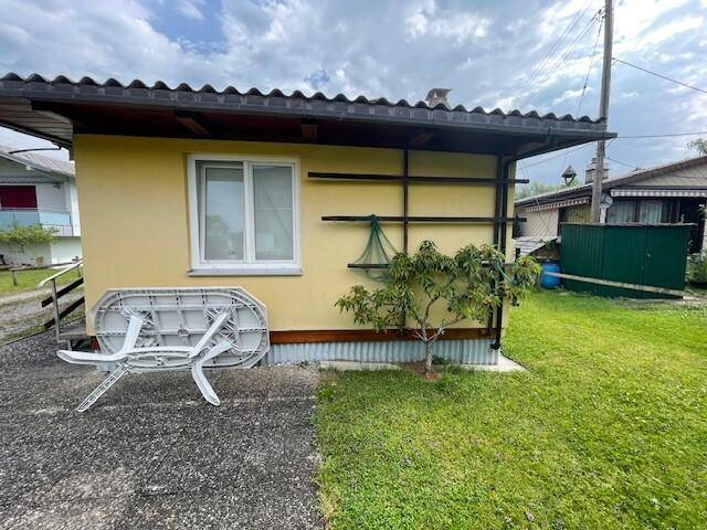 Seitenansicht des Hauses mit kleinem Baum, Rasen und einem Klapptisch im Freien.