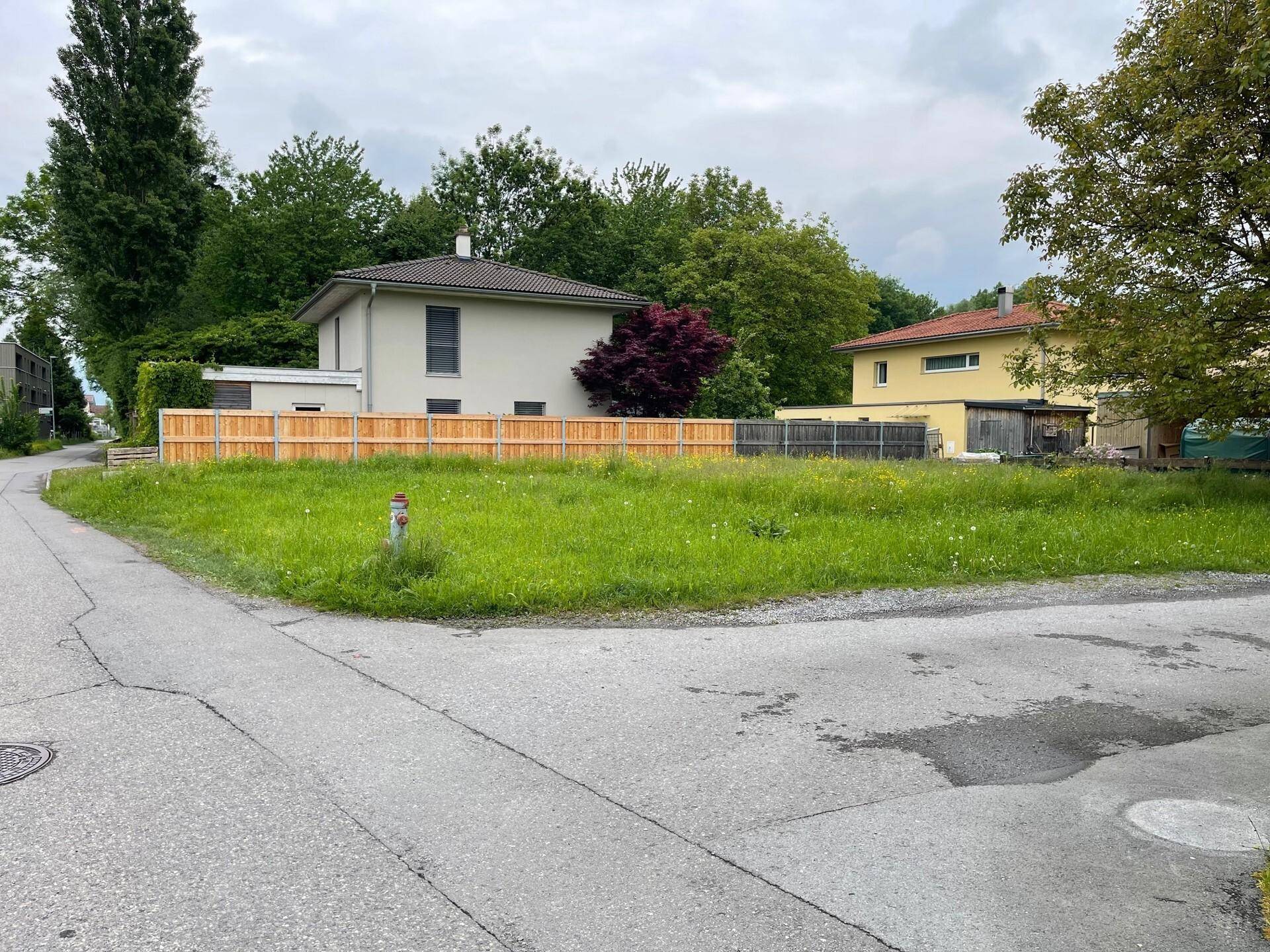 Grundstück mit Holzzaun und umliegenden Häusern an einem bewölkten Tag.