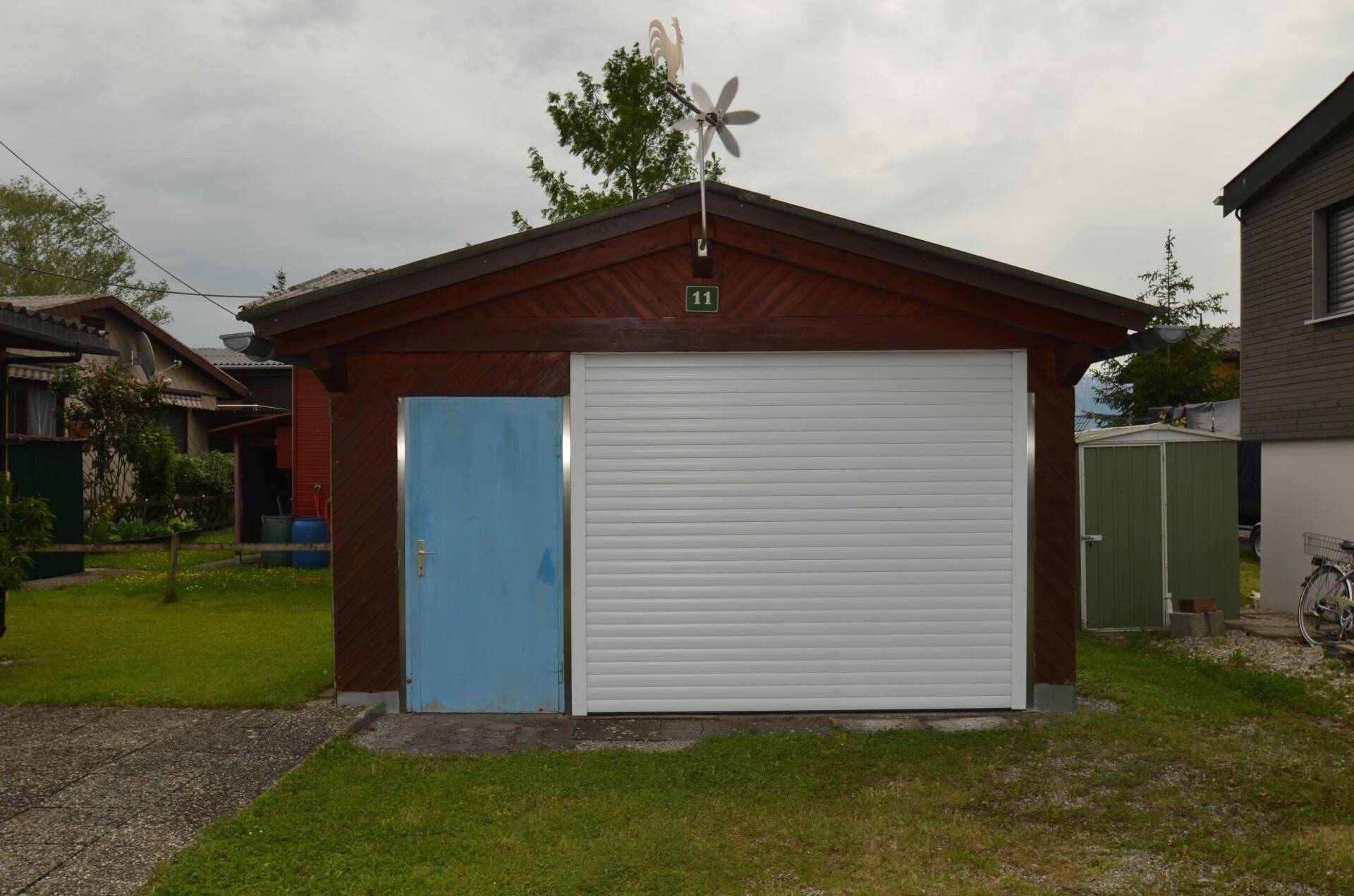 Separate Garage mit weißem Rolltor und blauer Tür neben dem Hauptgebäude.