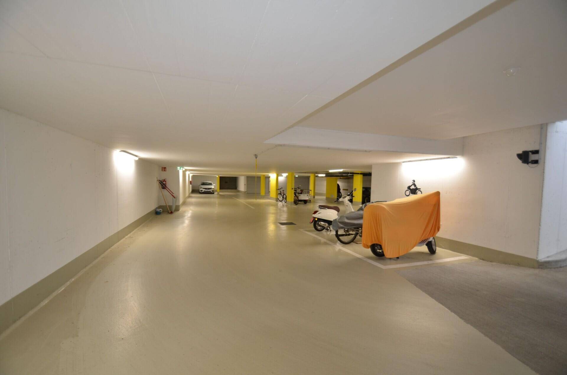 Langer Korridor in der Tiefgarage mit geparkten Motorrädern und guter Beleuchtung.